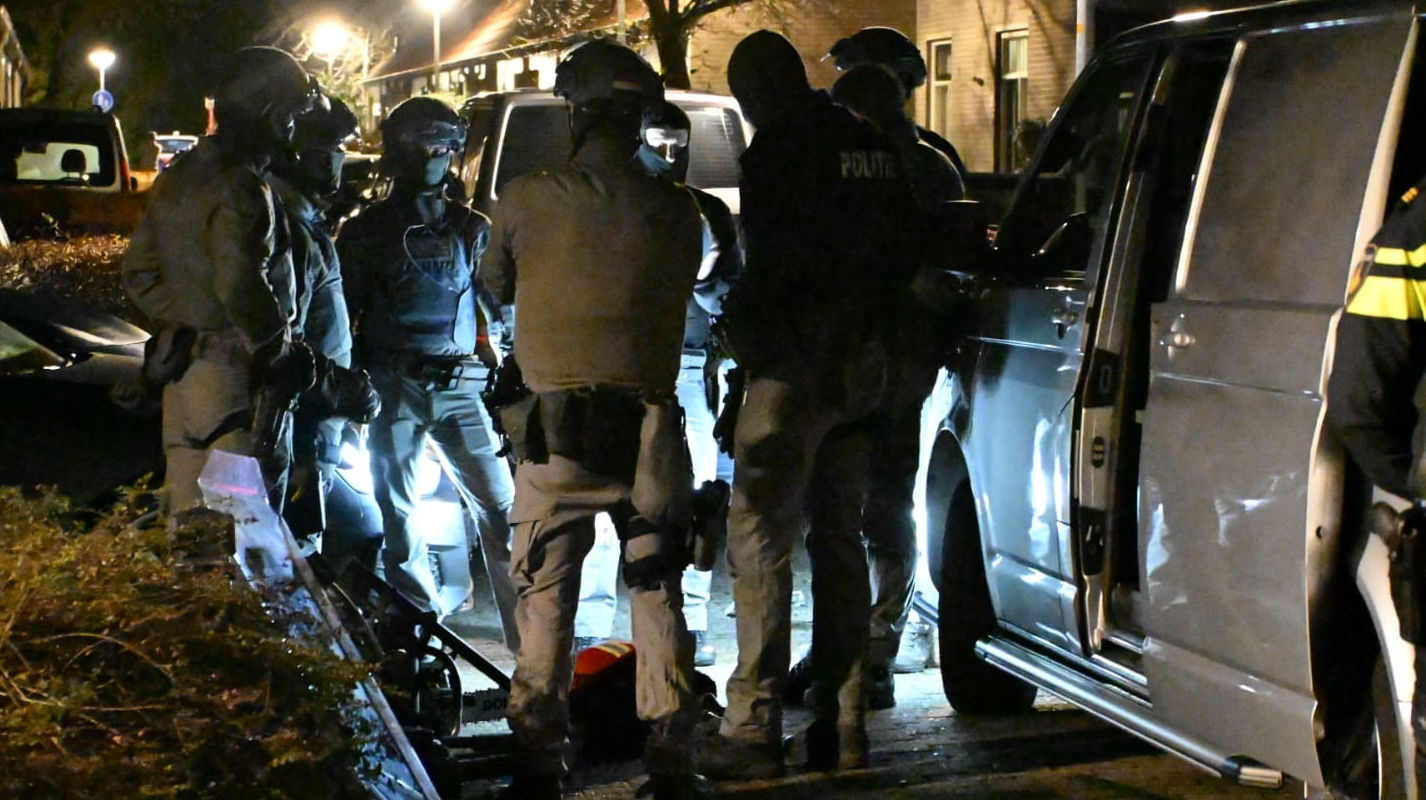 Gewapende politieagenten in tactische uitrusting staan 's nachts in een groep naast een bestelwagen op een straat.