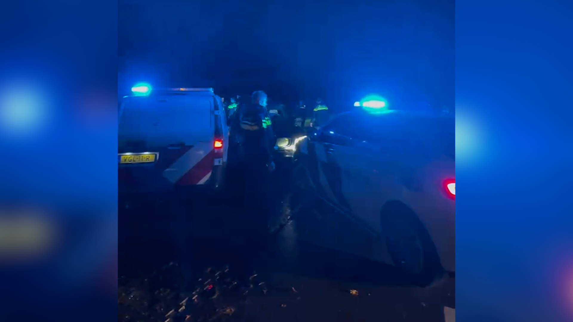 Politievoertuigen met zwaailichten aan staan stil in het donker, omgeven door enkele politieagenten.