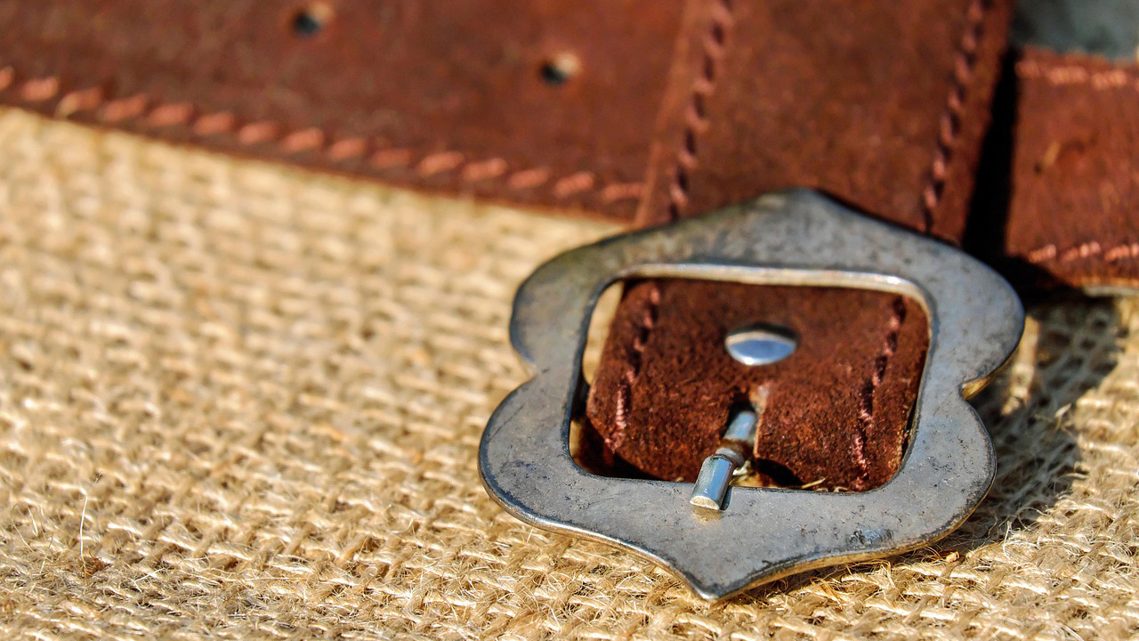 Close-up van een bruine leren riem met een metalen gesp, geplaatst op een juten achtergrond.