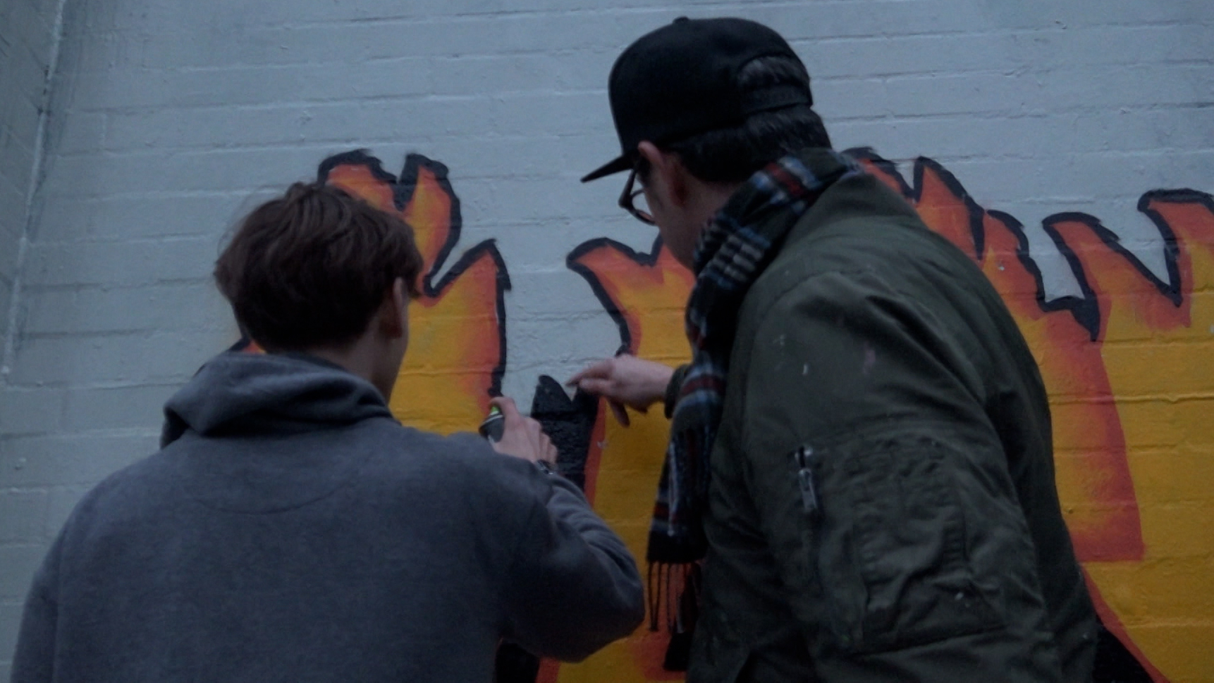 Twee mensen schilderen een kleurrijke muurschildering met vlammen op een muur.