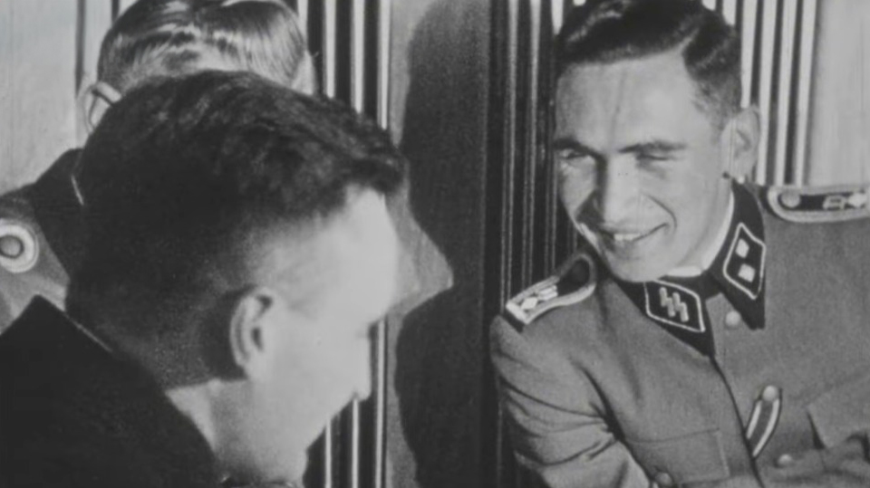 Twee mannen in SS-uniformen lachen en praten met elkaar in een zwart-witfoto.