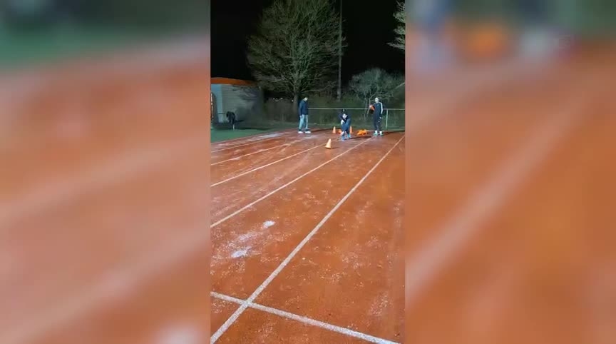 Mensen bereiden zich voor op een activiteit op een atletiekbaan 's nachts, bij een startpoort met kegels.