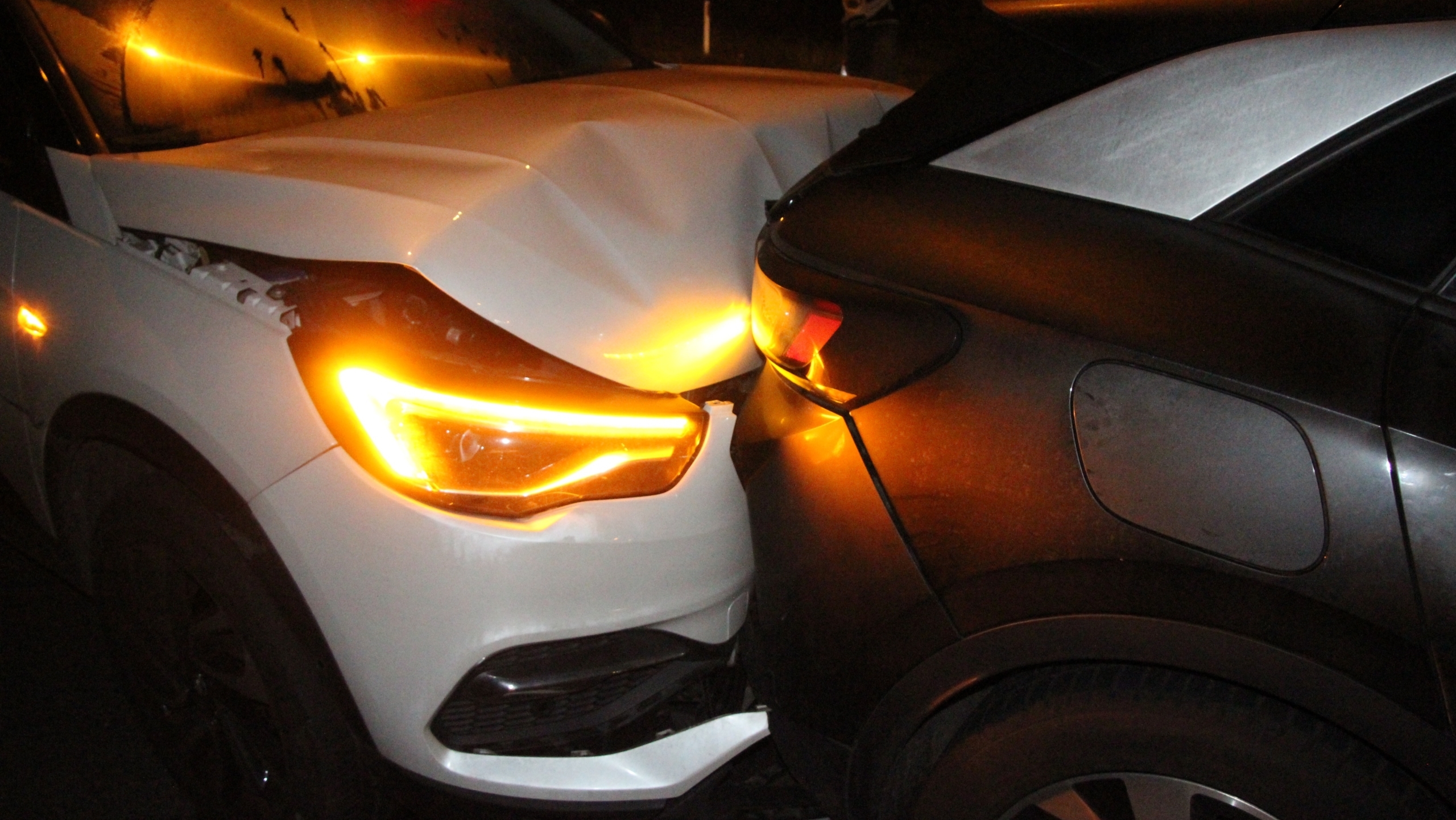 Twee auto's botsen tegen elkaar in het donker, met de voorkant van een witte auto beschadigd door de achterkant van een zwarte auto.