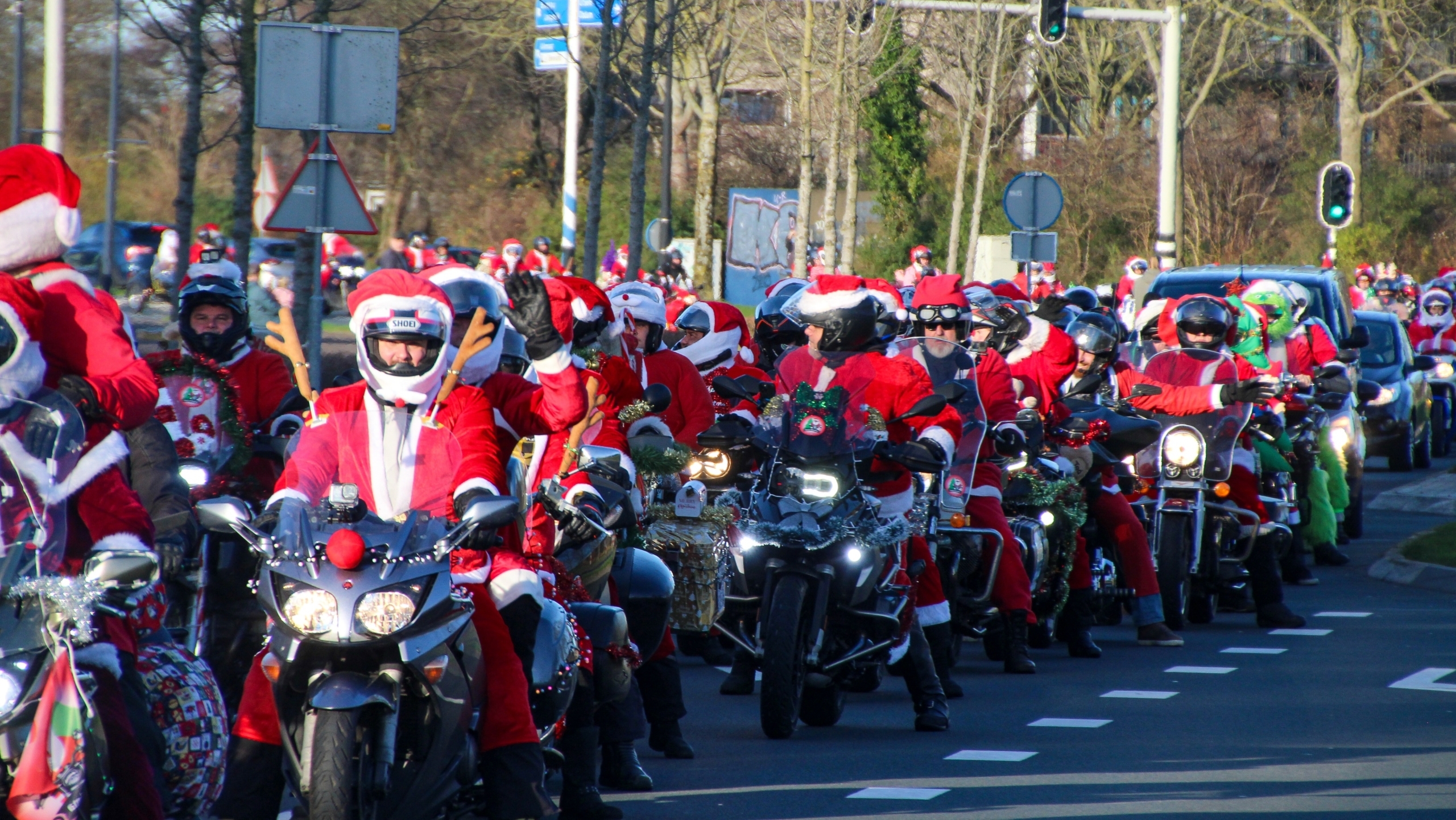 Een grote groep motorrijders gekleed in kerstmannenpakken rijdt op een rijbaan, met verschillende motoren versierd met kerstversieringen.