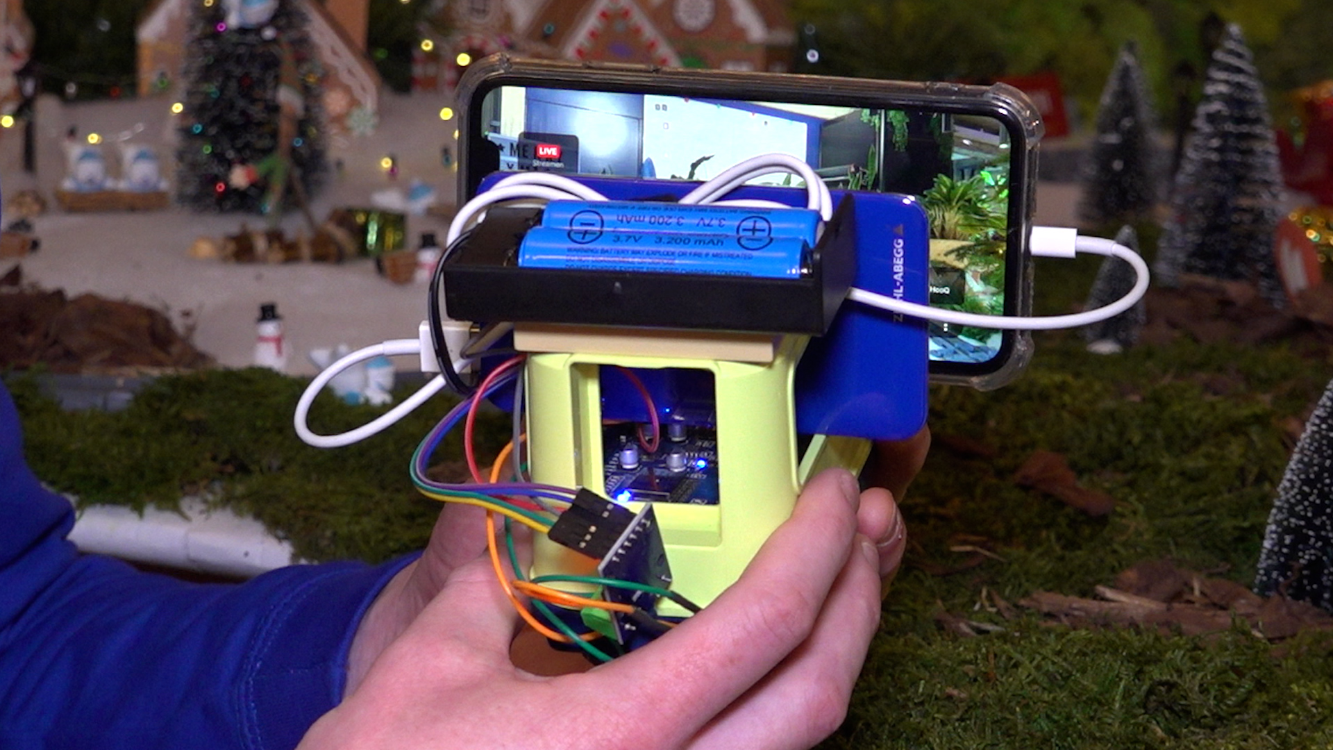 Handen houden een zelfgemaakt apparaat met een smartphone, batterijen en gekleurde draden.