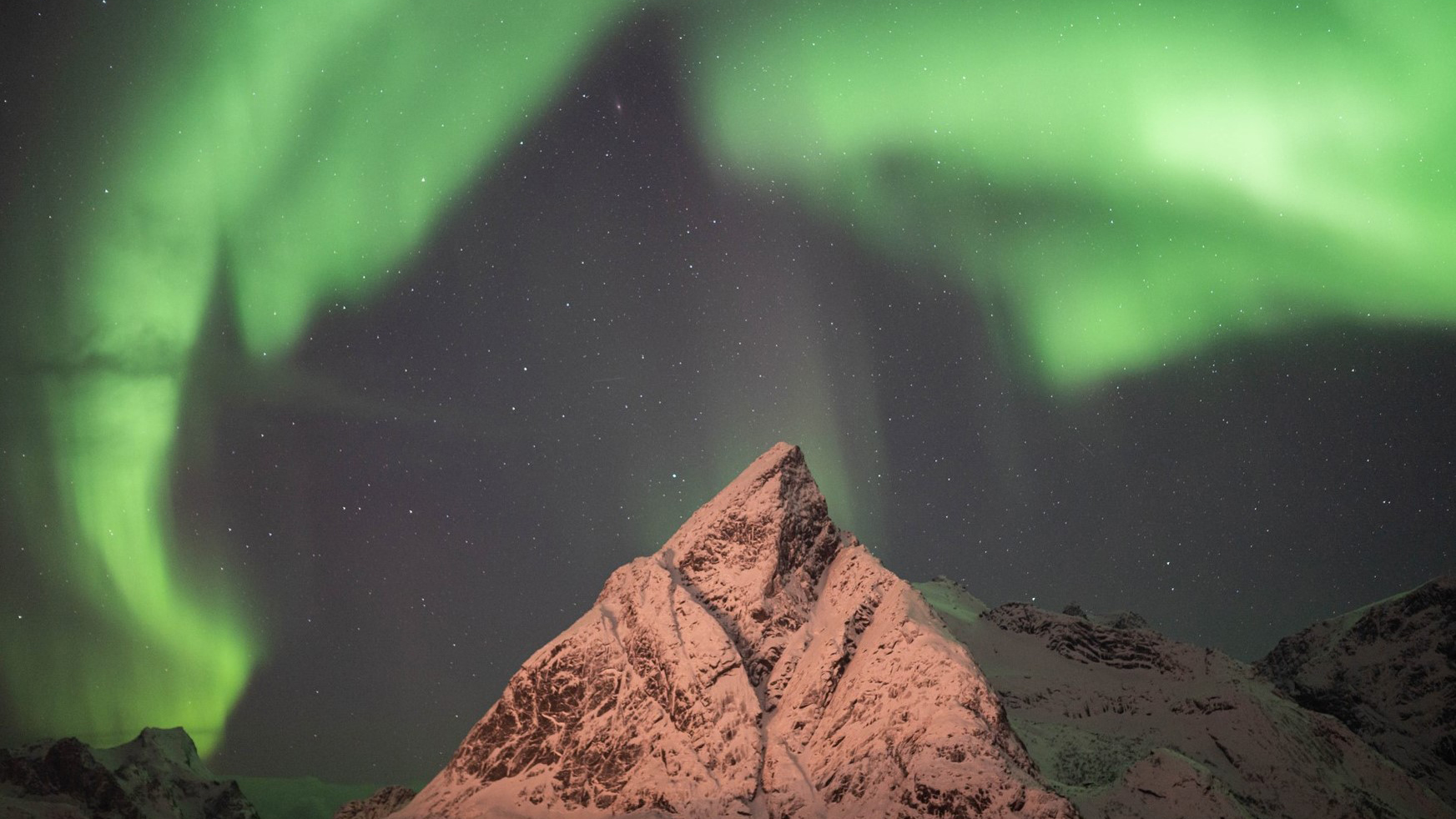 Sneeuwbedekte bergtop onder een groene aurora borealis aan een sterrenhemel.