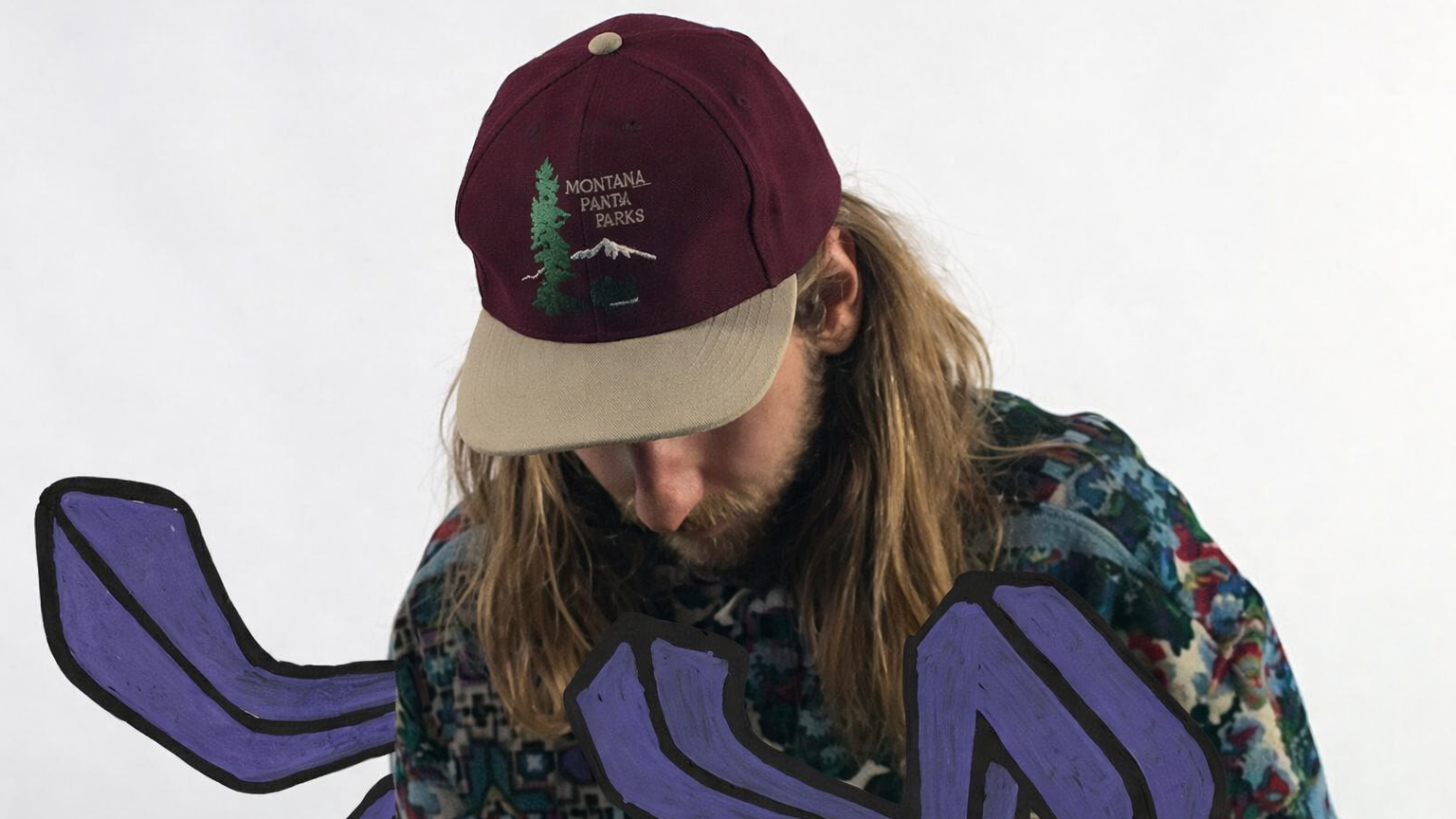 Man met lang haar draagt een pet en kleurrijk shirt, met paarse getekende elementen op de voorgrond.