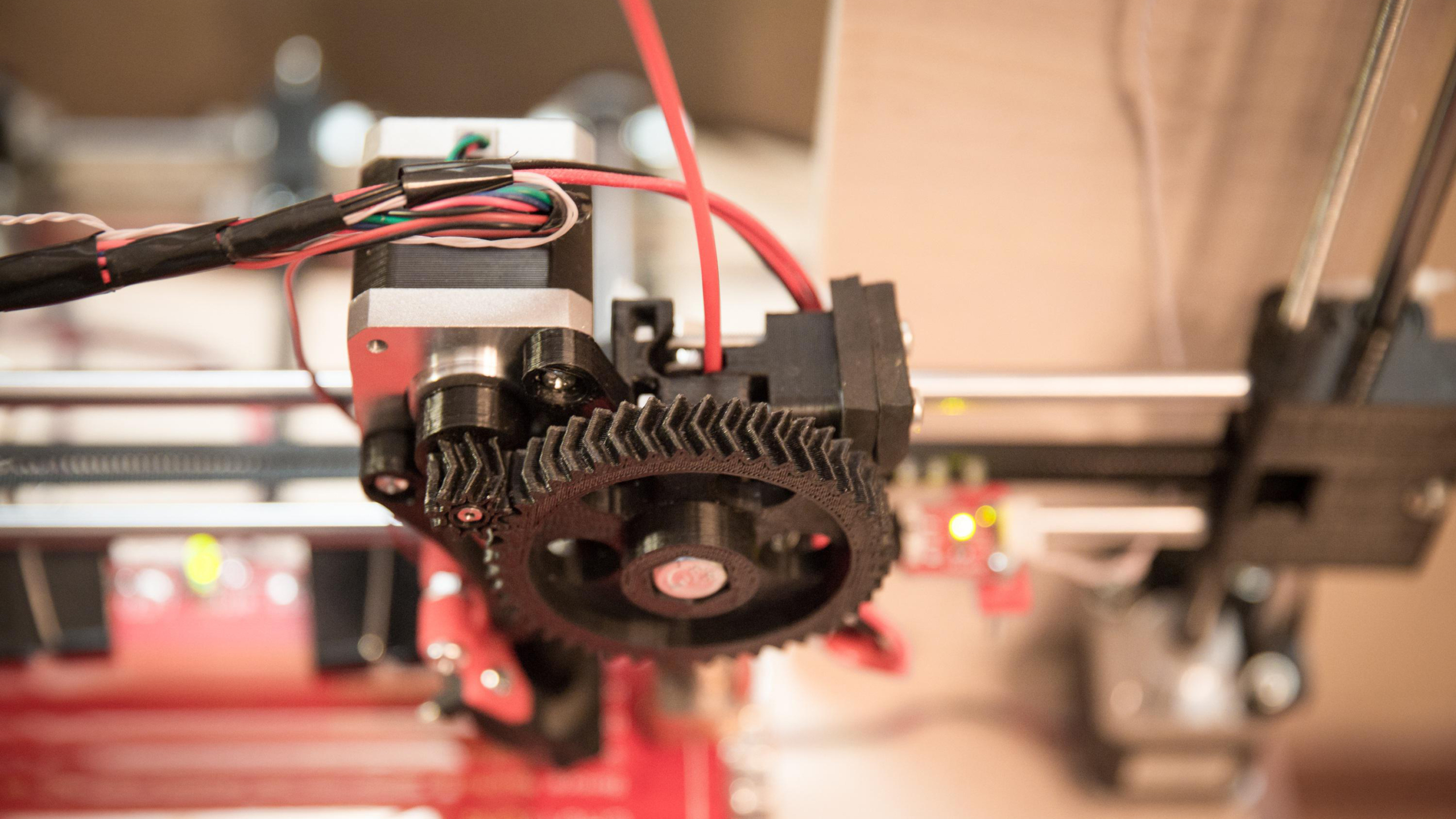 Close-up van een 3D-printermotor met zichtbare tandwielen en bedrading.