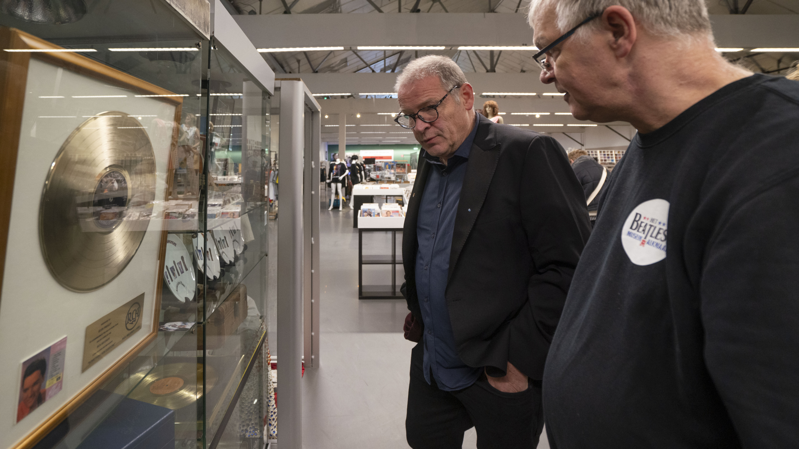 Twee mannen bekijken gouden platen in een vitrine in een tentoonstellingsruimte.