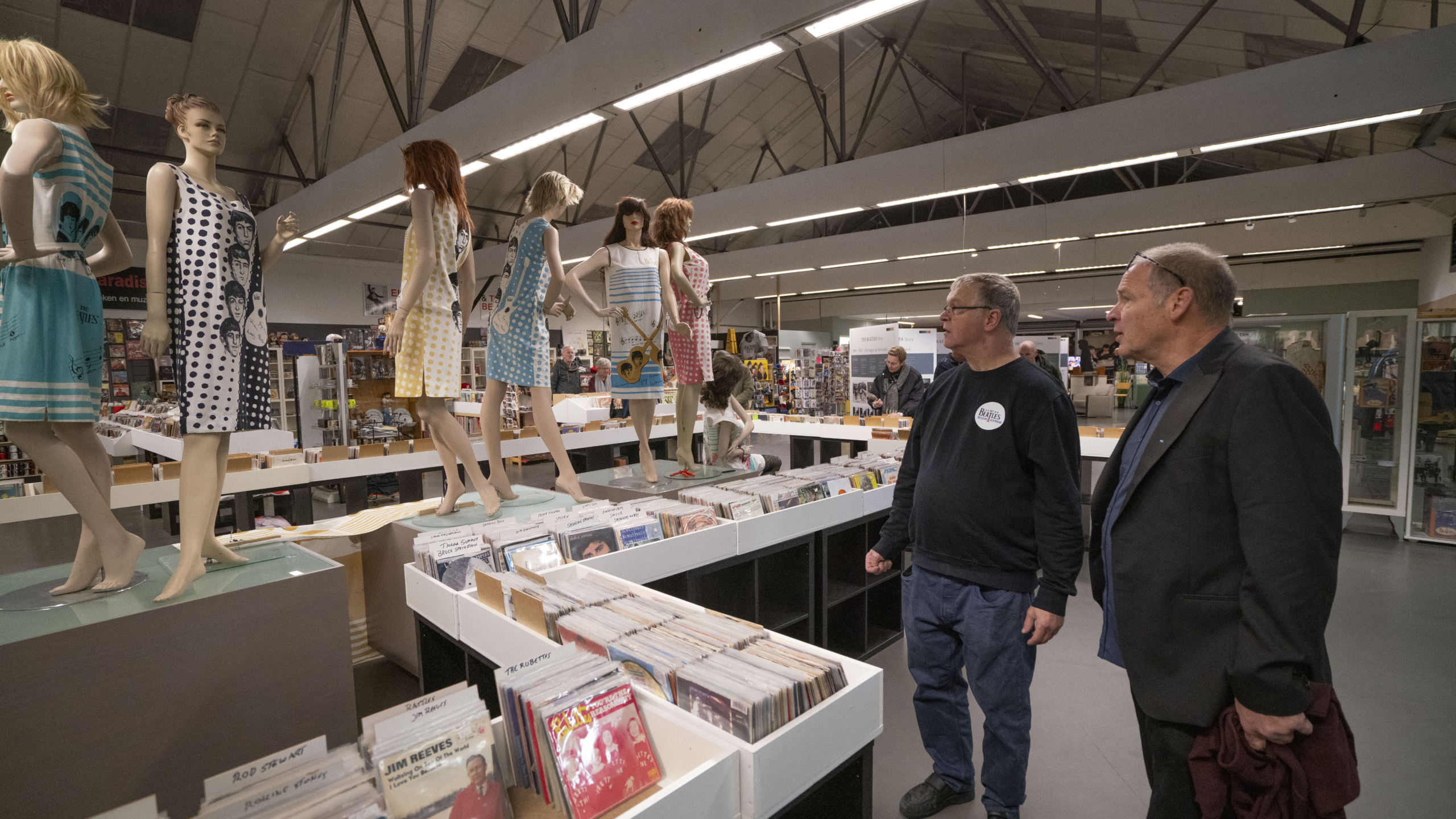 Mensen kijken naar poppen in retro jurken in een winkel met muziekalbums en platen in de rekken.