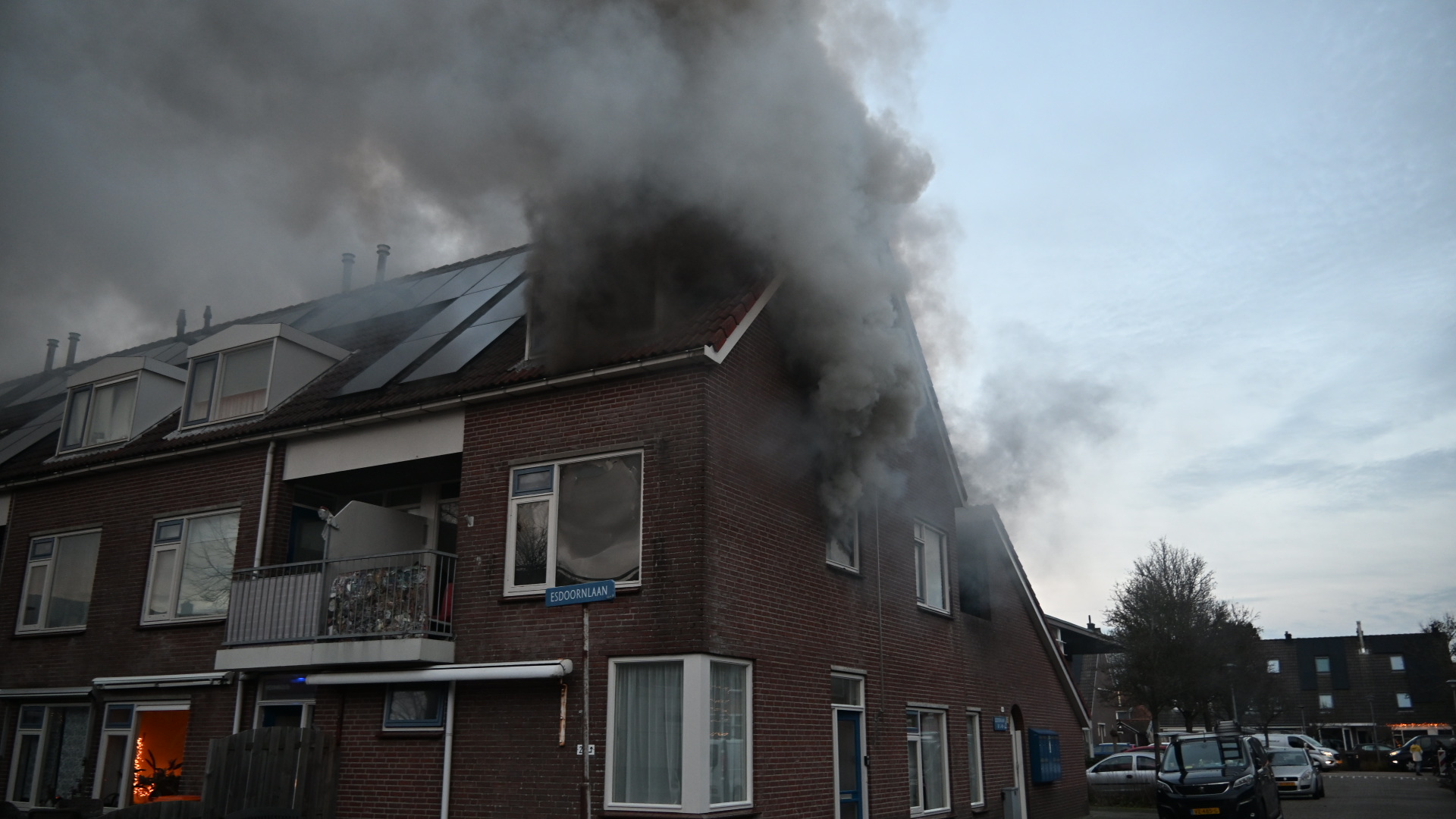 Rook stijgt op uit het dak van een hoekwoning met zonnepanelen, aan straat Esdoornlaan.