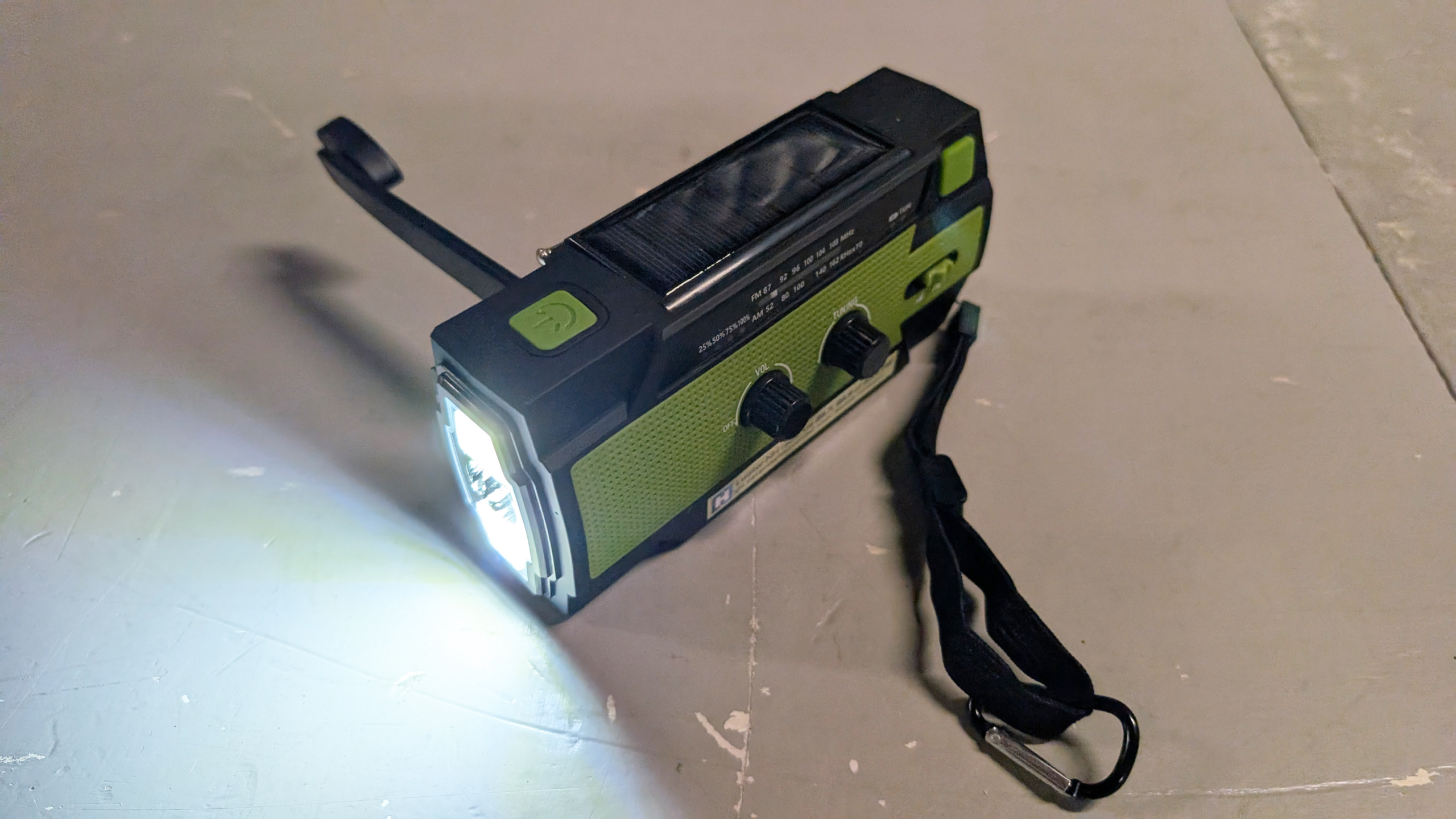 Zaklamp met een ingebouwde radio en opwindhendel, groen en zwart, ligt op een vloer met het licht ingeschakeld.