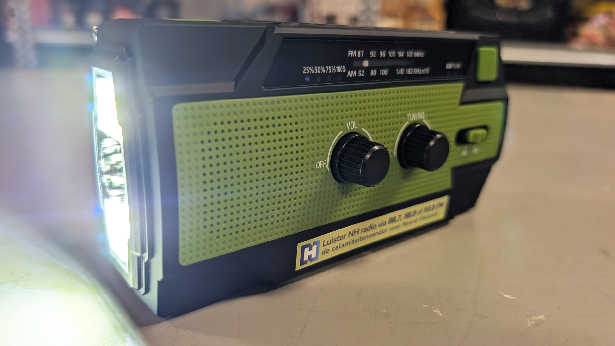 Groene draagbare radio met volumeknop en afstemknop, met een ingeschakelde zaklamp aan de linkerzijde.