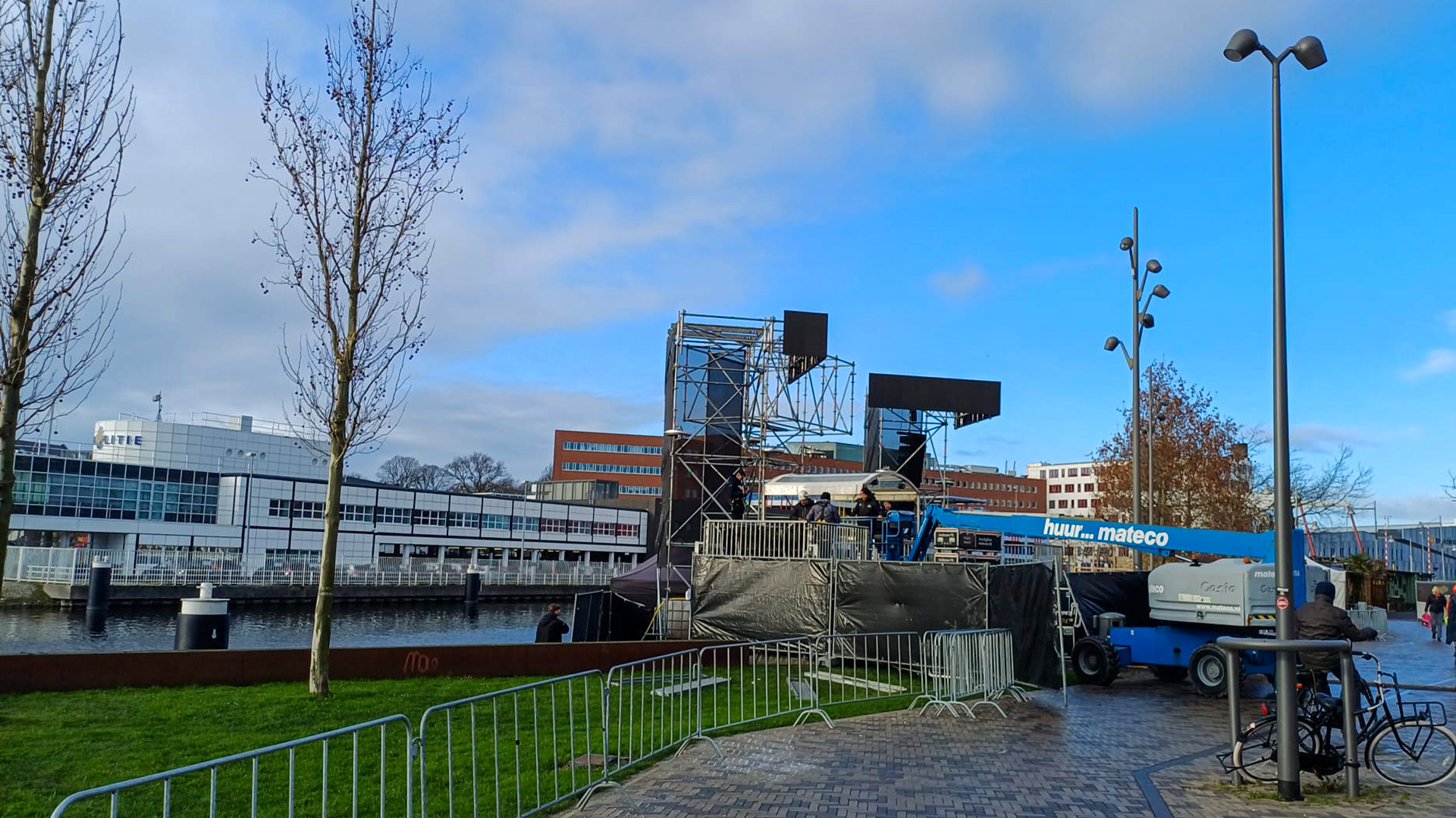 Een kraan met opbouwconstructie naast een water en kantoorgebouw met blauwe lucht op de achtergrond.