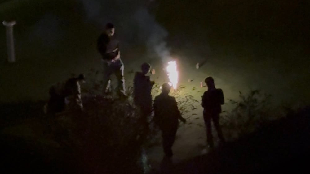 Groep mensen rond vuurwerk in het donker, omringd door schaduwen en rook.