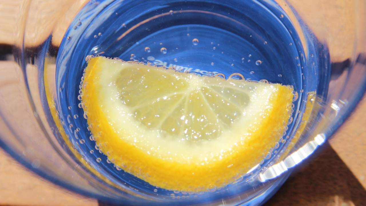 Een schijfje citroen in blaasjesrijk water met een blauwe gloed in een glas.