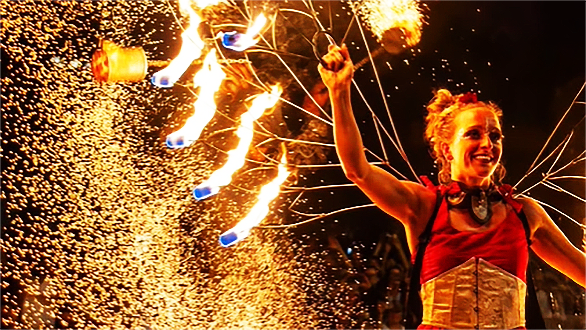 Vrouwelijk vuurartiest met een kleurrijke fontein van vonken en vlammende strengen op de achtergrond.