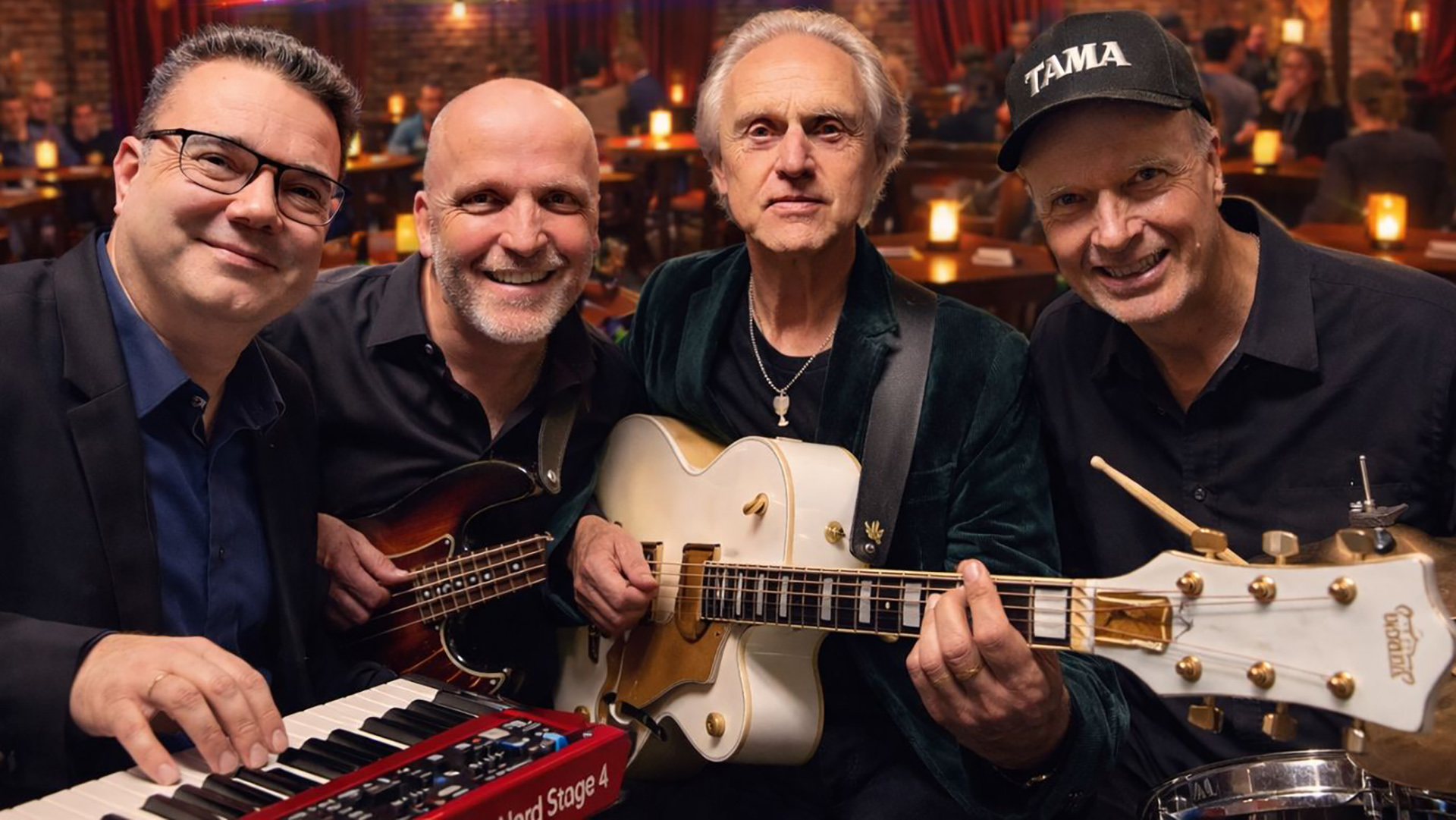 Vier mannen poseren met muziekinstrumenten in een sfeervol café, met een keyboard, basgitaar en drumstel op de voorgrond.