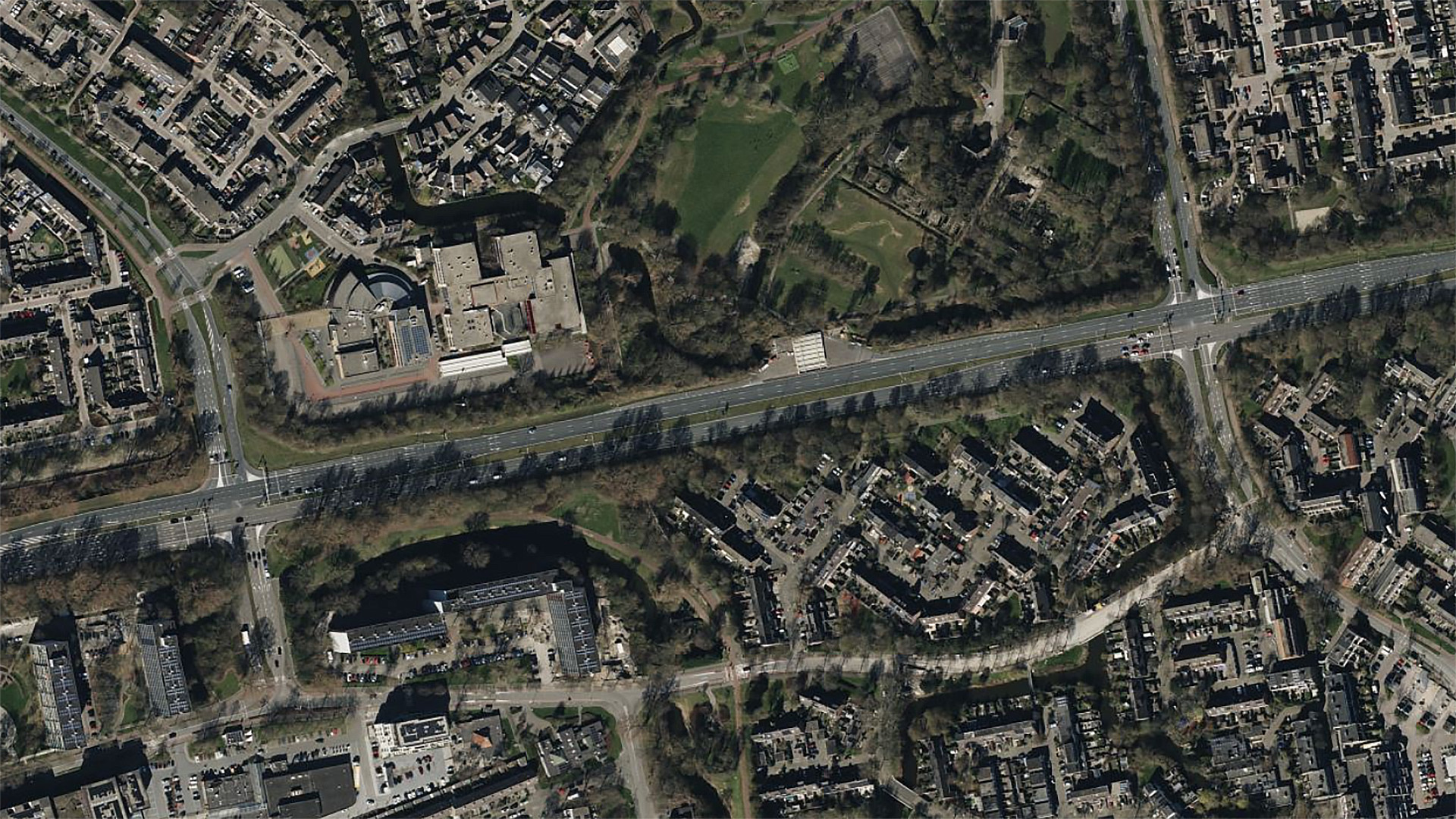 Luchtfoto van een stedelijk gebied met wegen, gebouwen en een park aan de bovenkant.