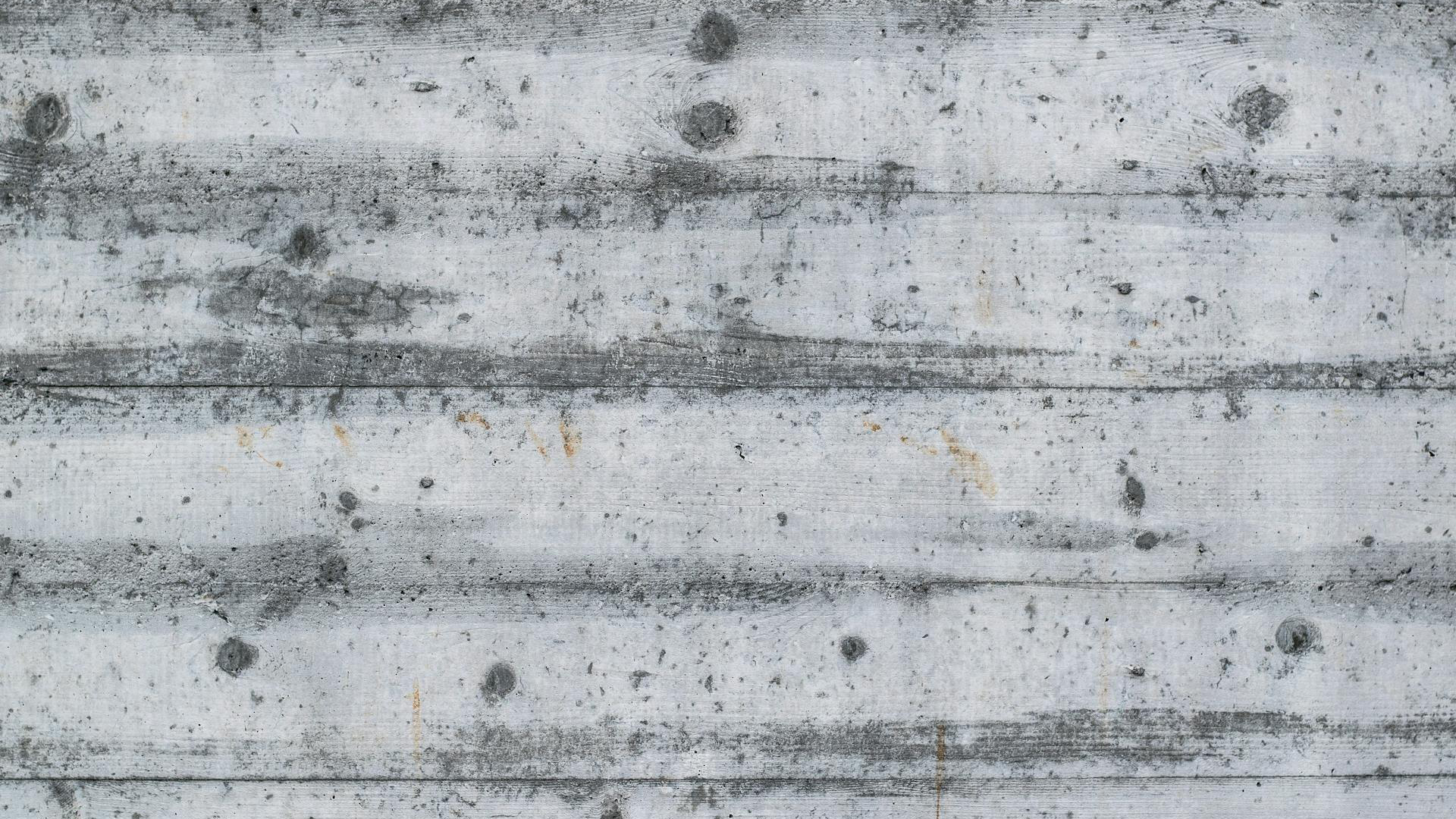 Grijze betonnen muur met horizontale planken en zichtbare textuur en knoesten.