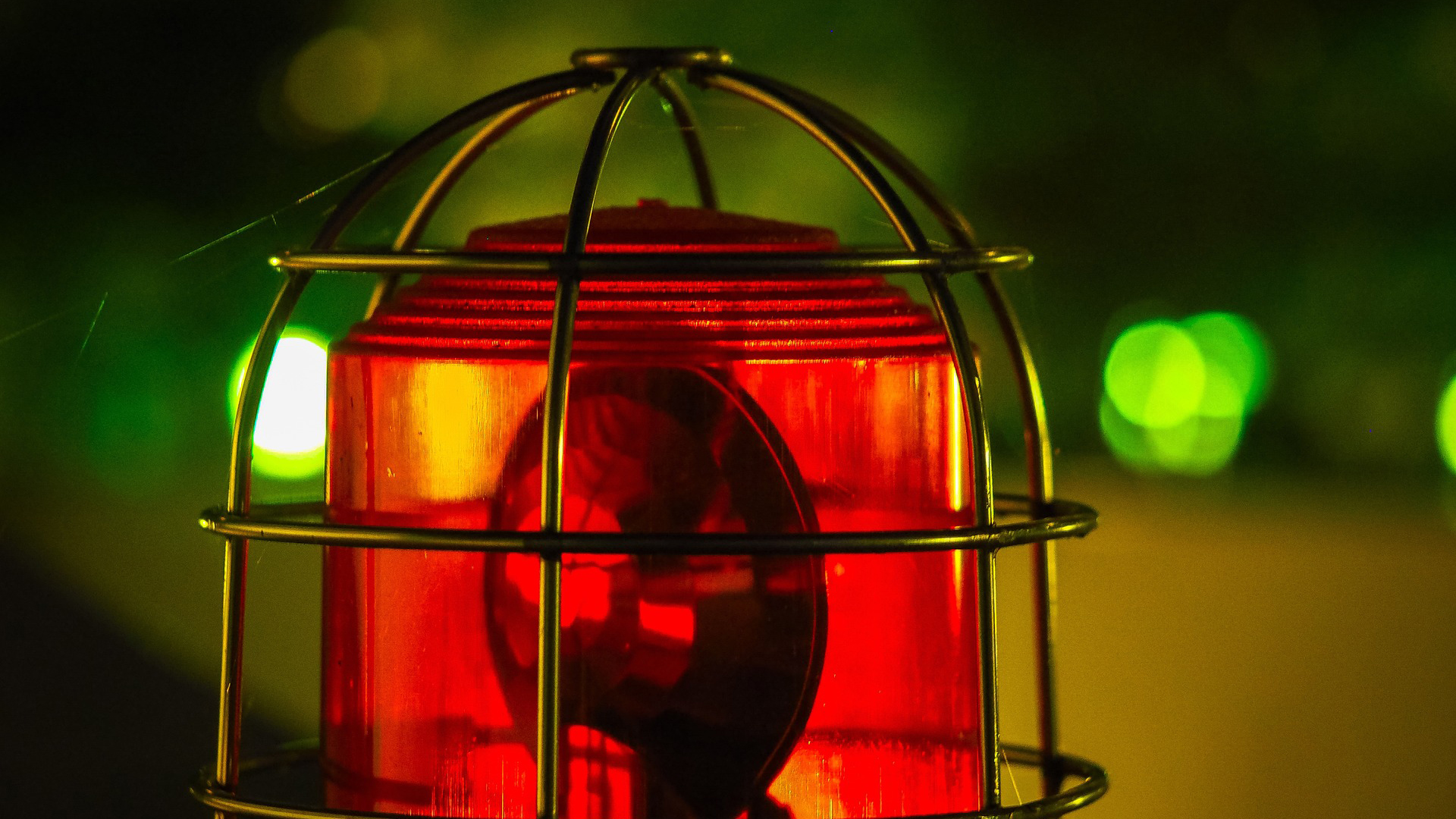 Rood waarschuwingslicht in een metalen kooi met groene bokeh lichten op de achtergrond.