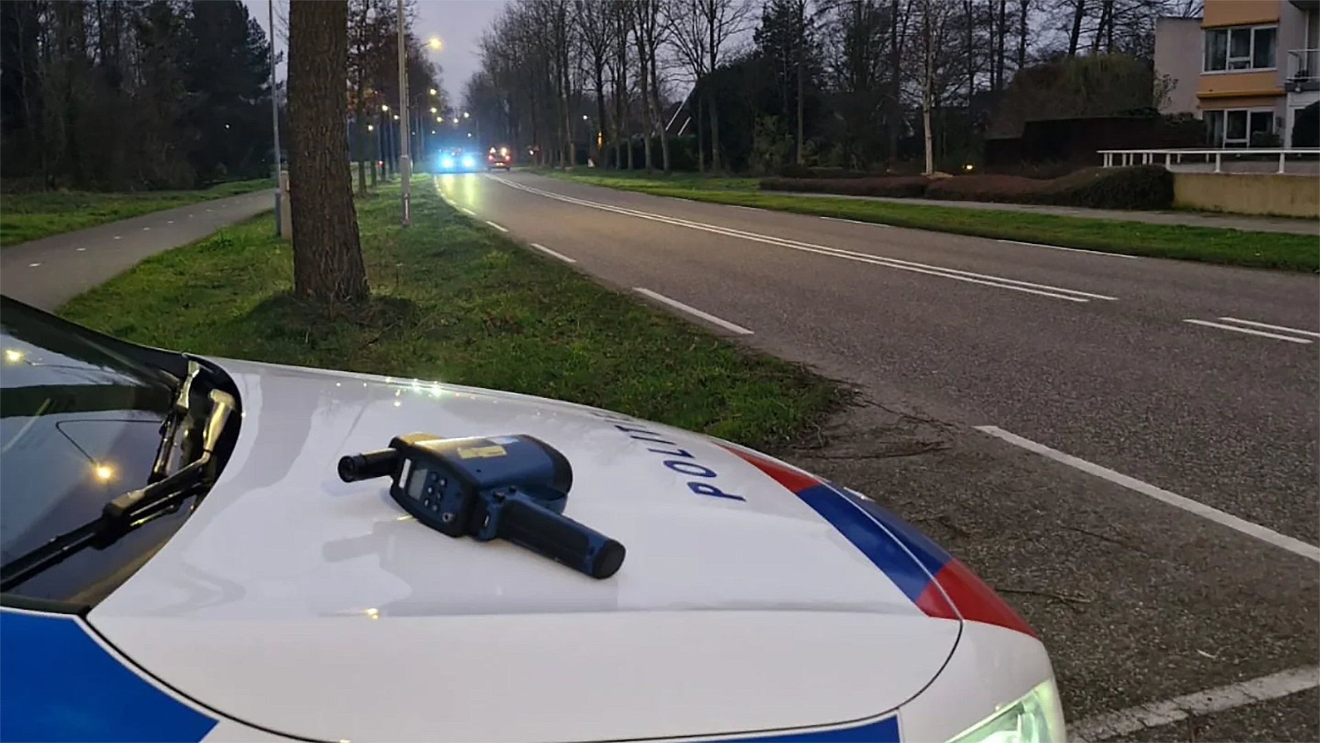 Snelheidsradar op de motorkap van een politieauto aan de kant van een weg bij schemering.