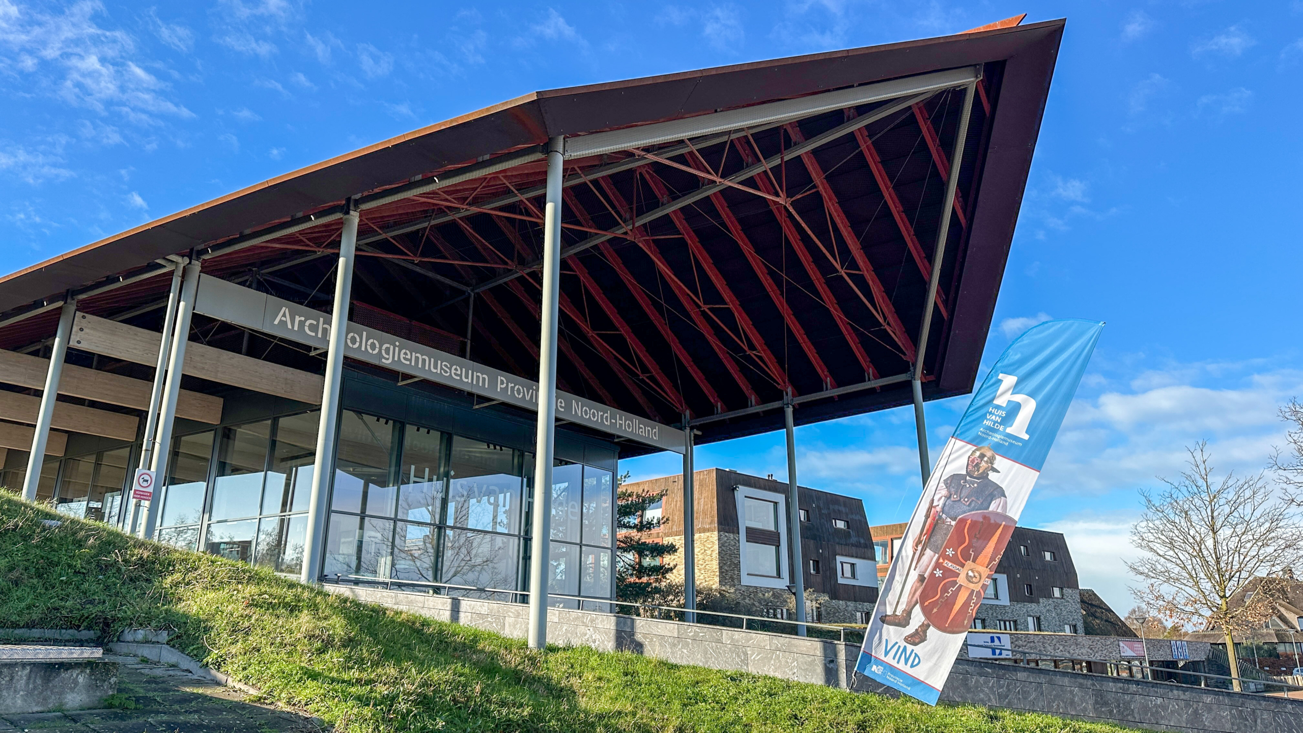 Entree van het Archeologiemuseum Provincie Noord-Holland met een opvallende luifel en een vlag met Romeins thema.