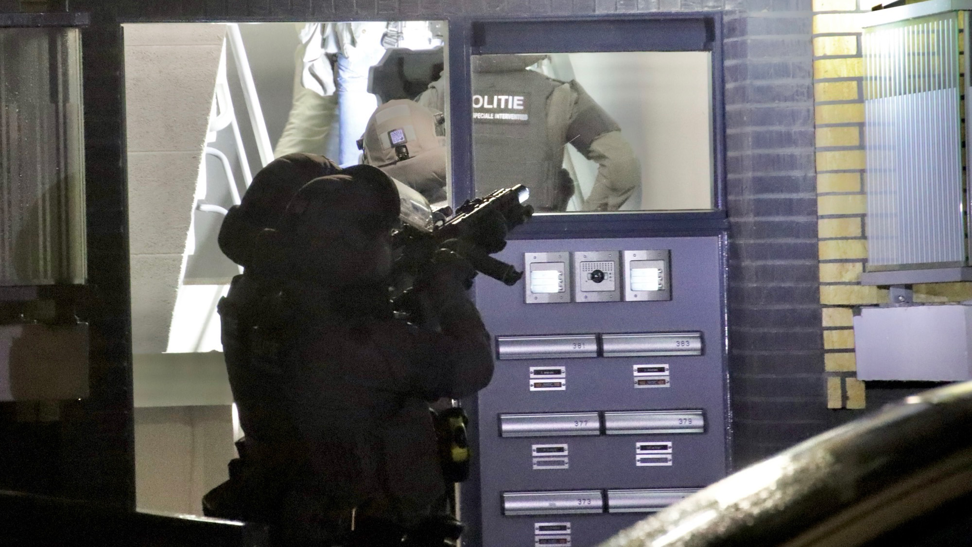 Gewapende politieagenten met speciale uitrusting voor een gebouw met postvakken, tijdens een operatie.