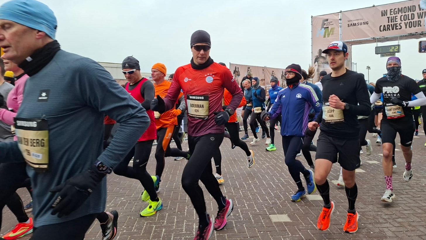 Groep hardlopers in sportkleding tijdens een wedstrijd op een bewolkte dag, met starttijd 22 minuten op de achtergrond.