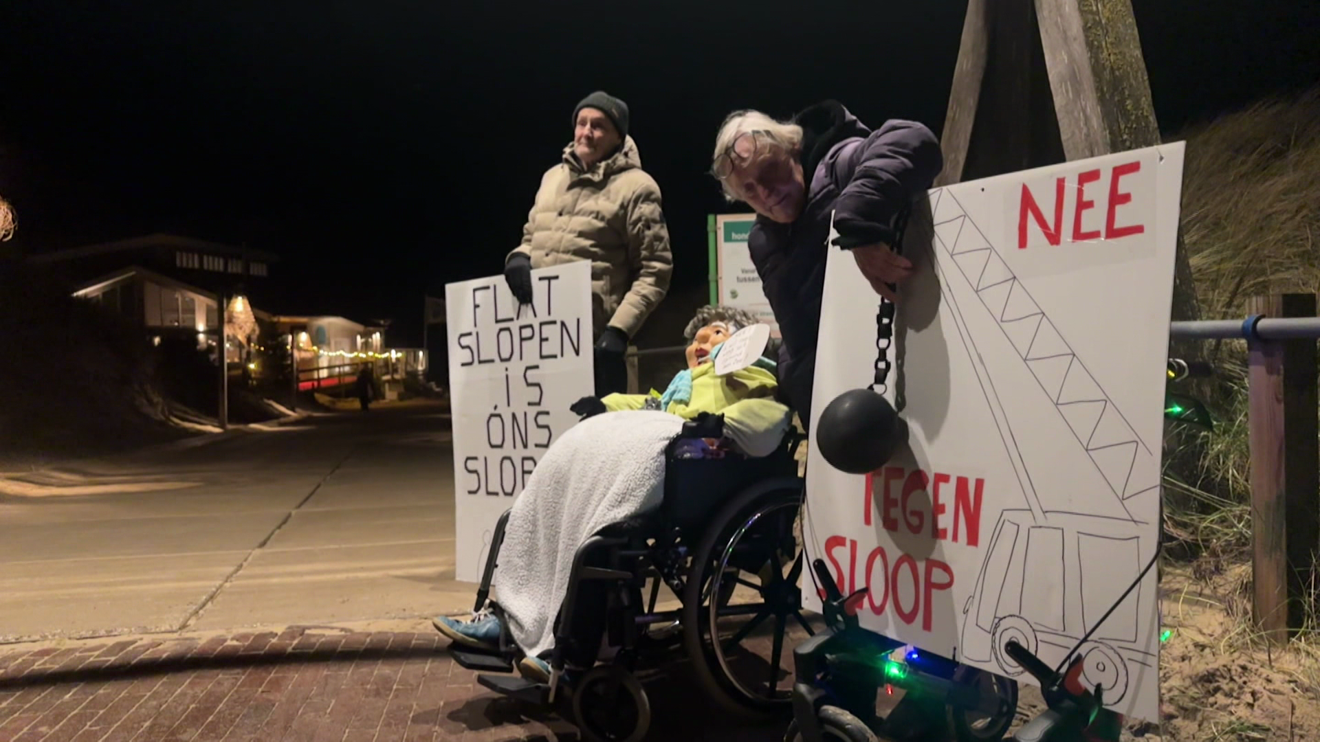 Twee personen protesteren 's avonds tegen de sloop, met borden met teksten als "Flat slopen is ons slopen".