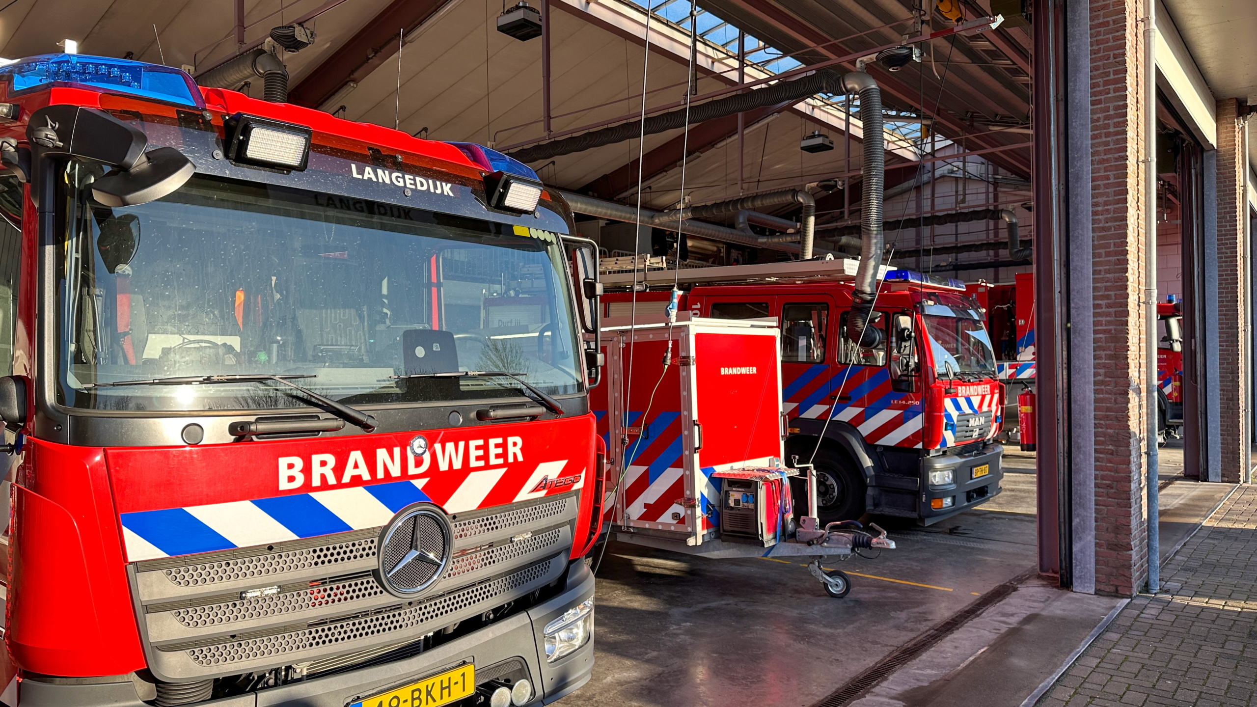 Rode brandweerwagens staan geparkeerd in een brandweerkazerne, met blauwe lampen en opvallende strepen.
