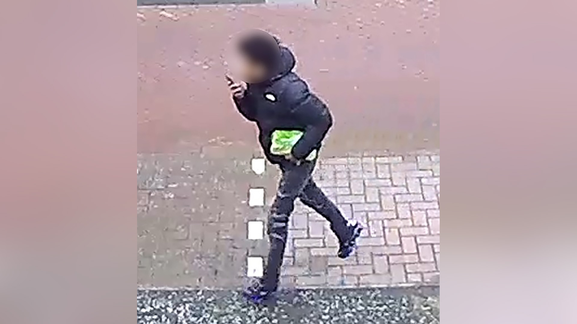 Persoon in zwarte jas loopt buiten met groene tas in de hand en telefoon tegen zijn oor.