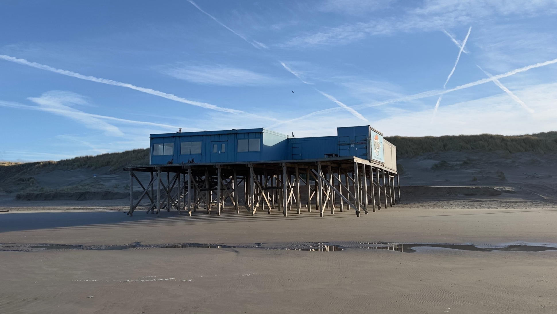 Stelgebouw op een rustig strand met blauwe lucht en wolkenstrepen.