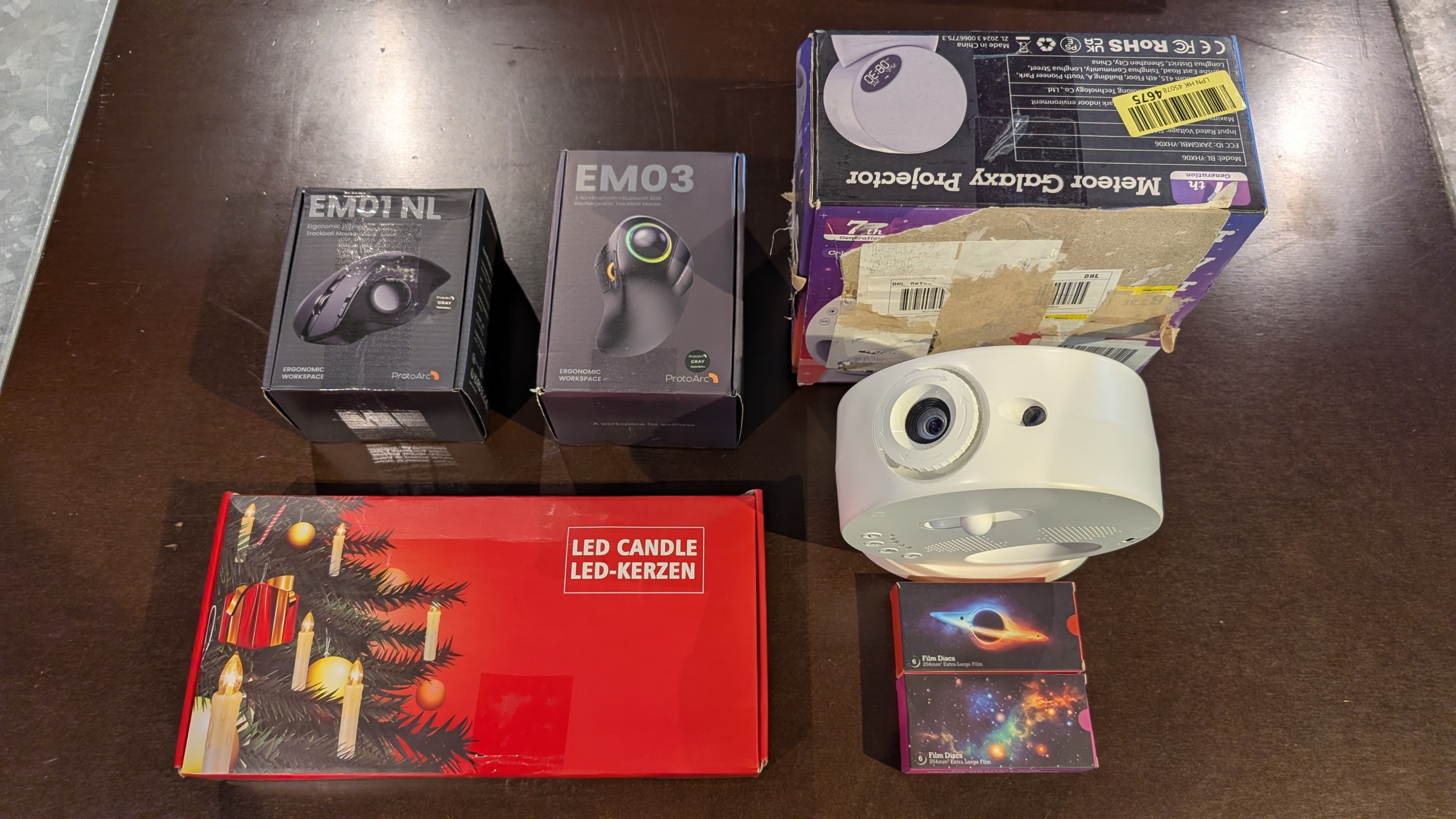 Diverse dozen op een tafel: een ergonomische muis, een LED-kaars, een projector, en een camera met filmdozen.