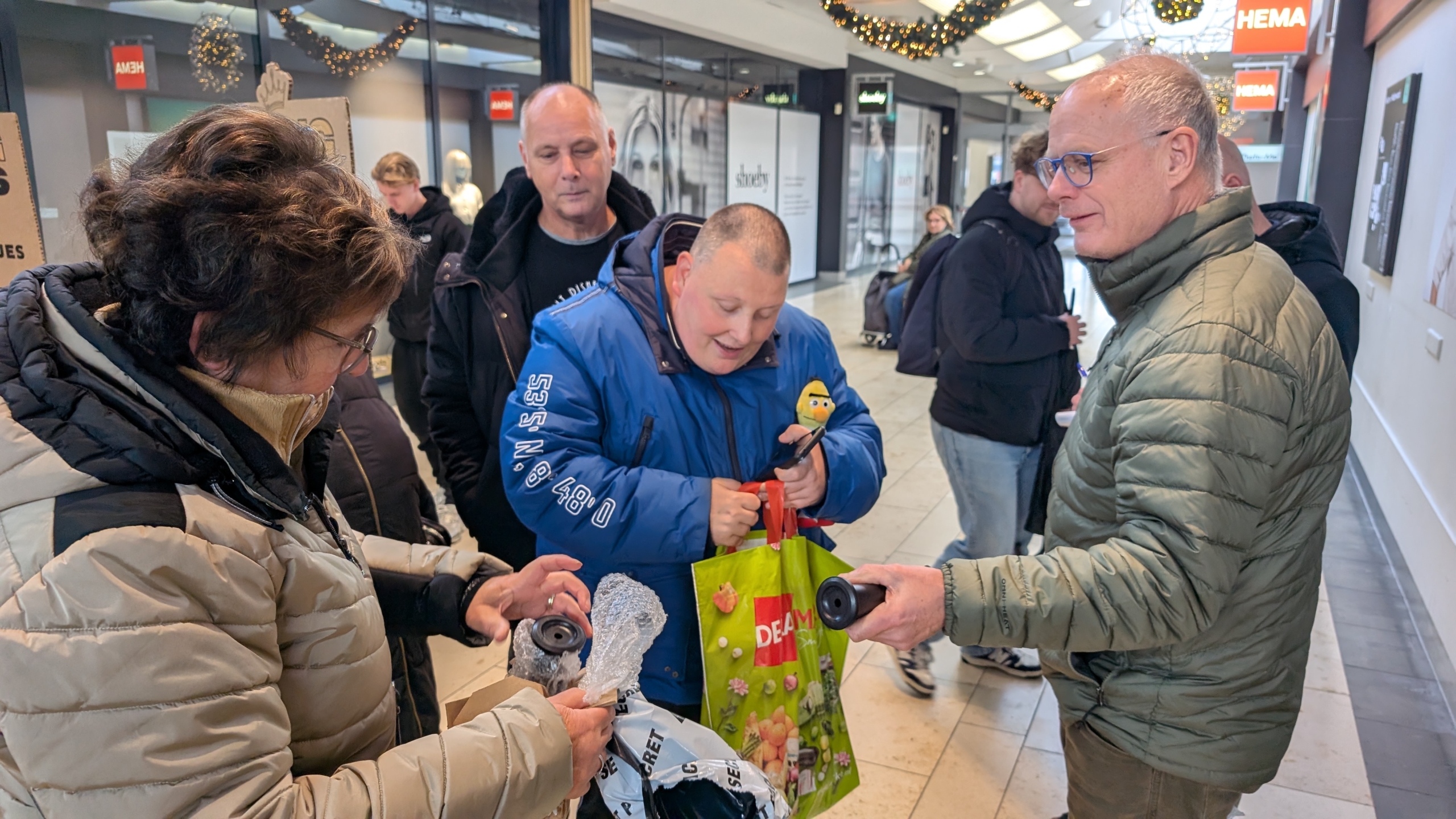 Mensen in een winkelcentrum wisselen voorwerpen uit, omgeven door kerstdecoraties.