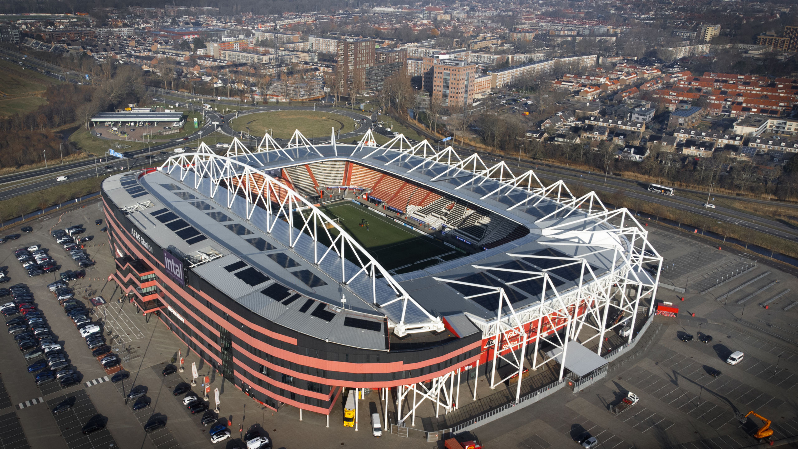 Luchtopname van het AFAS Stadion met de leegte van de parkeerplaatsen en omliggende stad en wegen.
