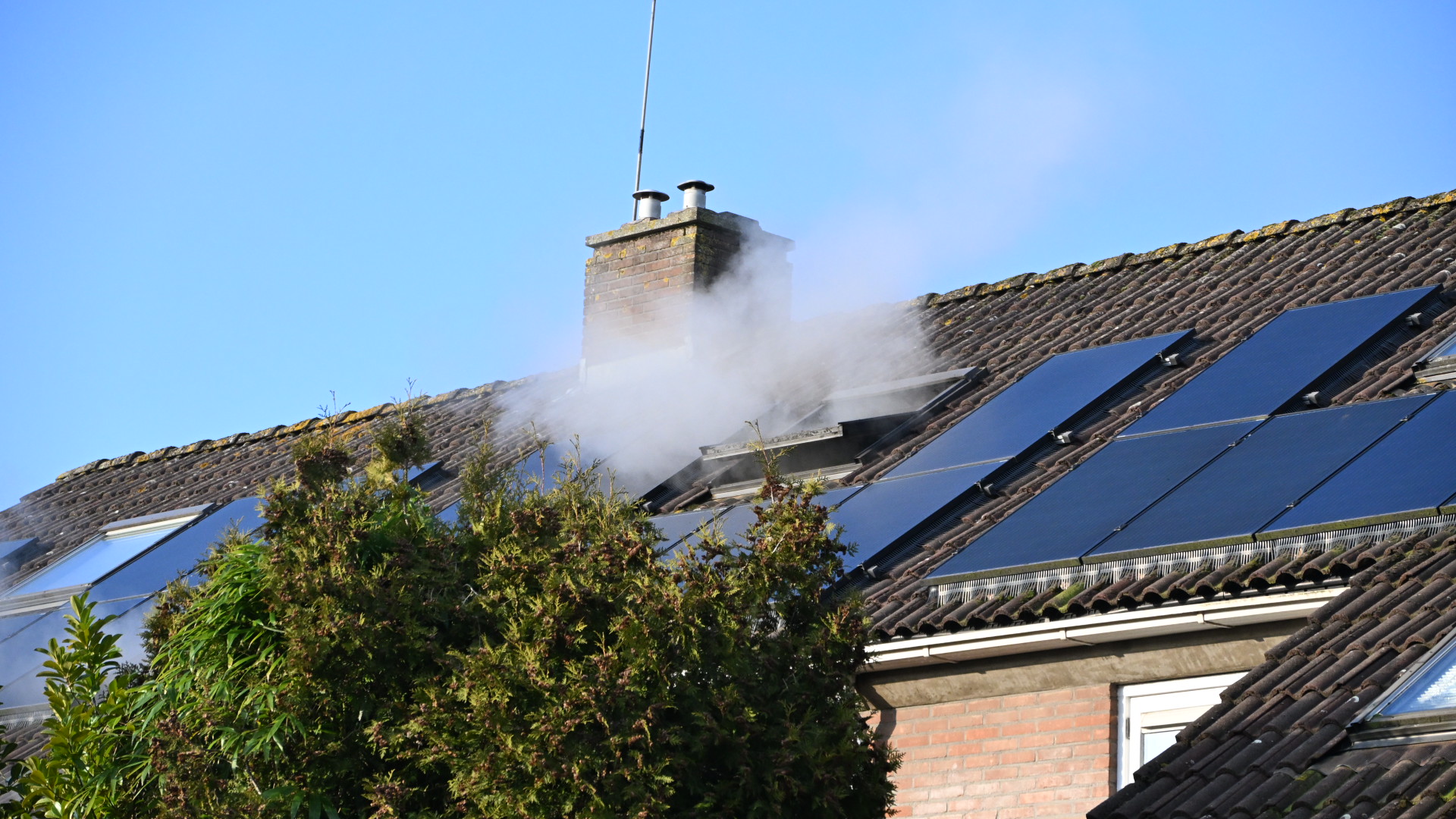 Rook stijgt op uit een schoorsteen van een huis met zonnepanelen op het dak.