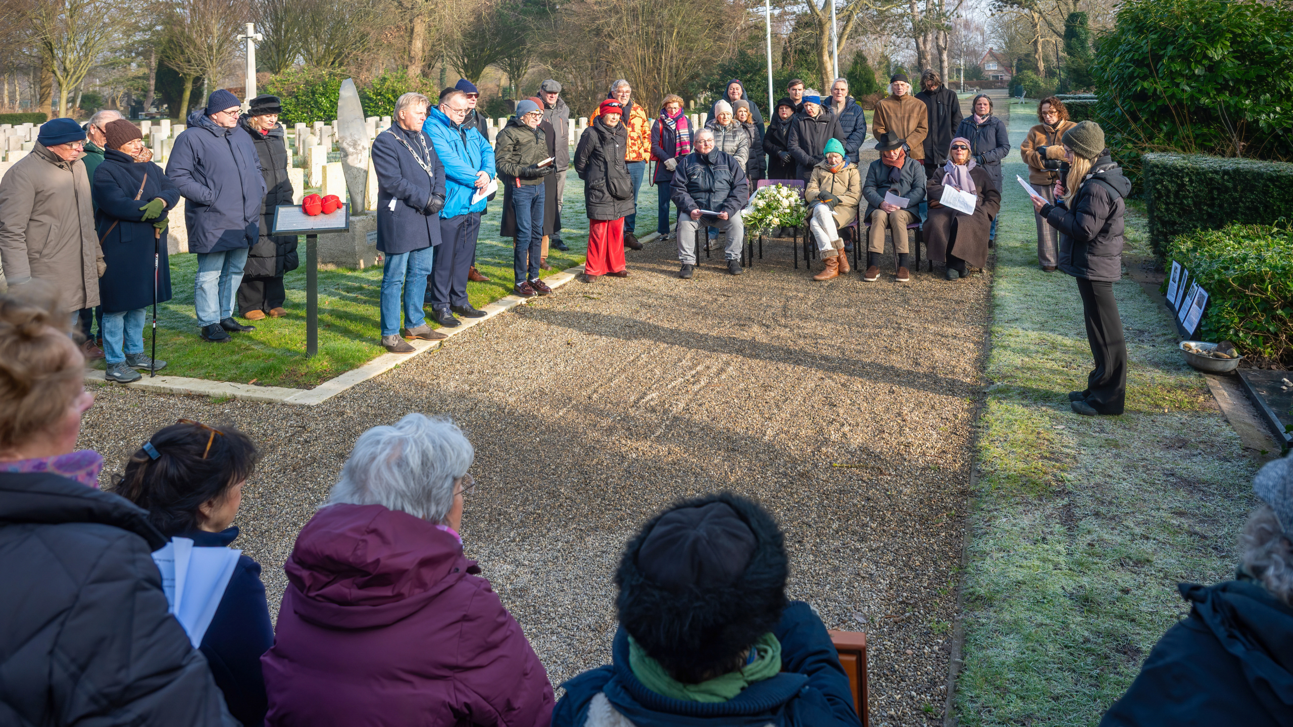 Een groep mensen verzameld bij een begraafplaats voor een ceremonie op een zonnige dag.