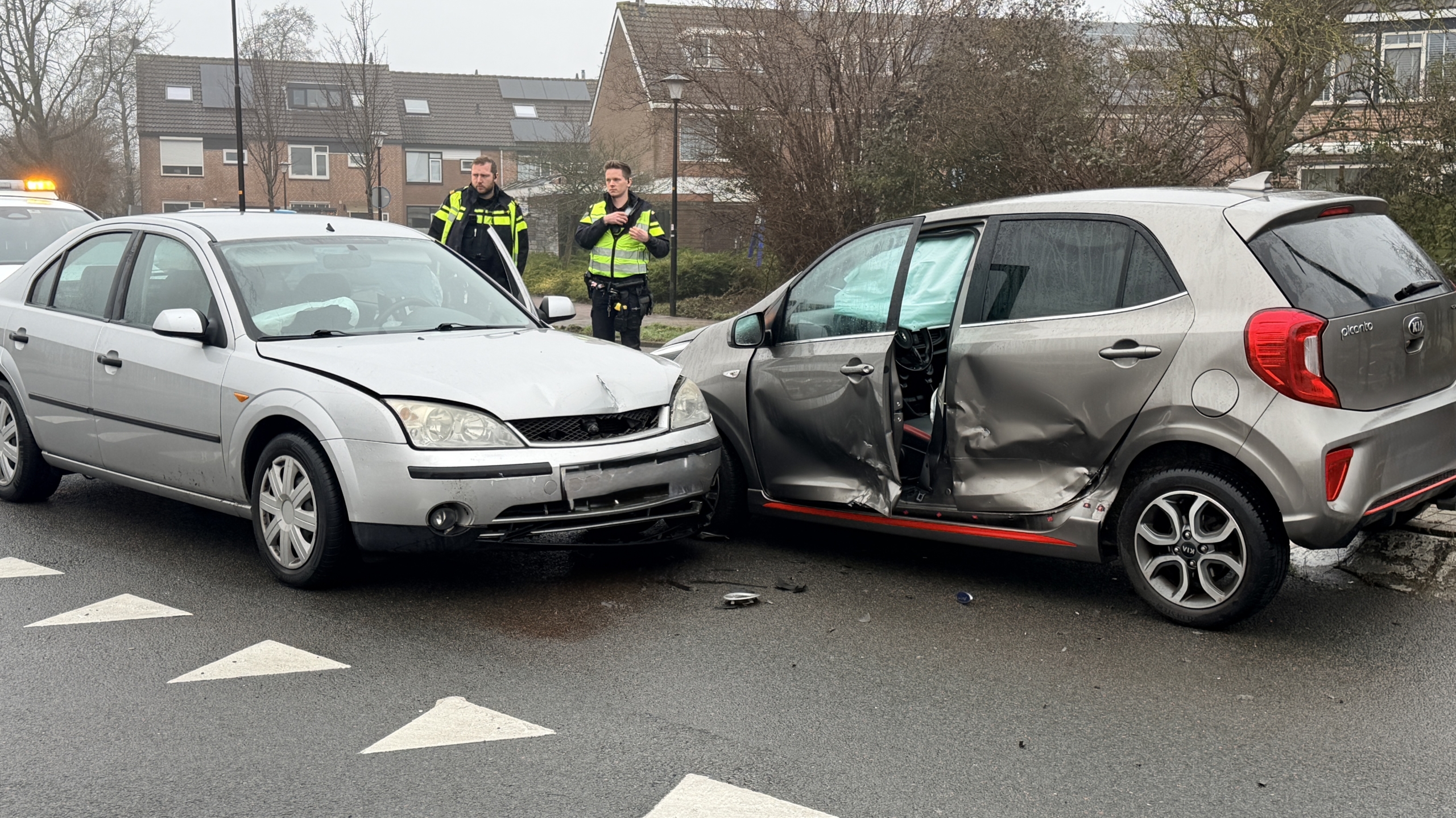 Twee auto's met schade na een botsing, met politieagenten die de situatie bekijken.