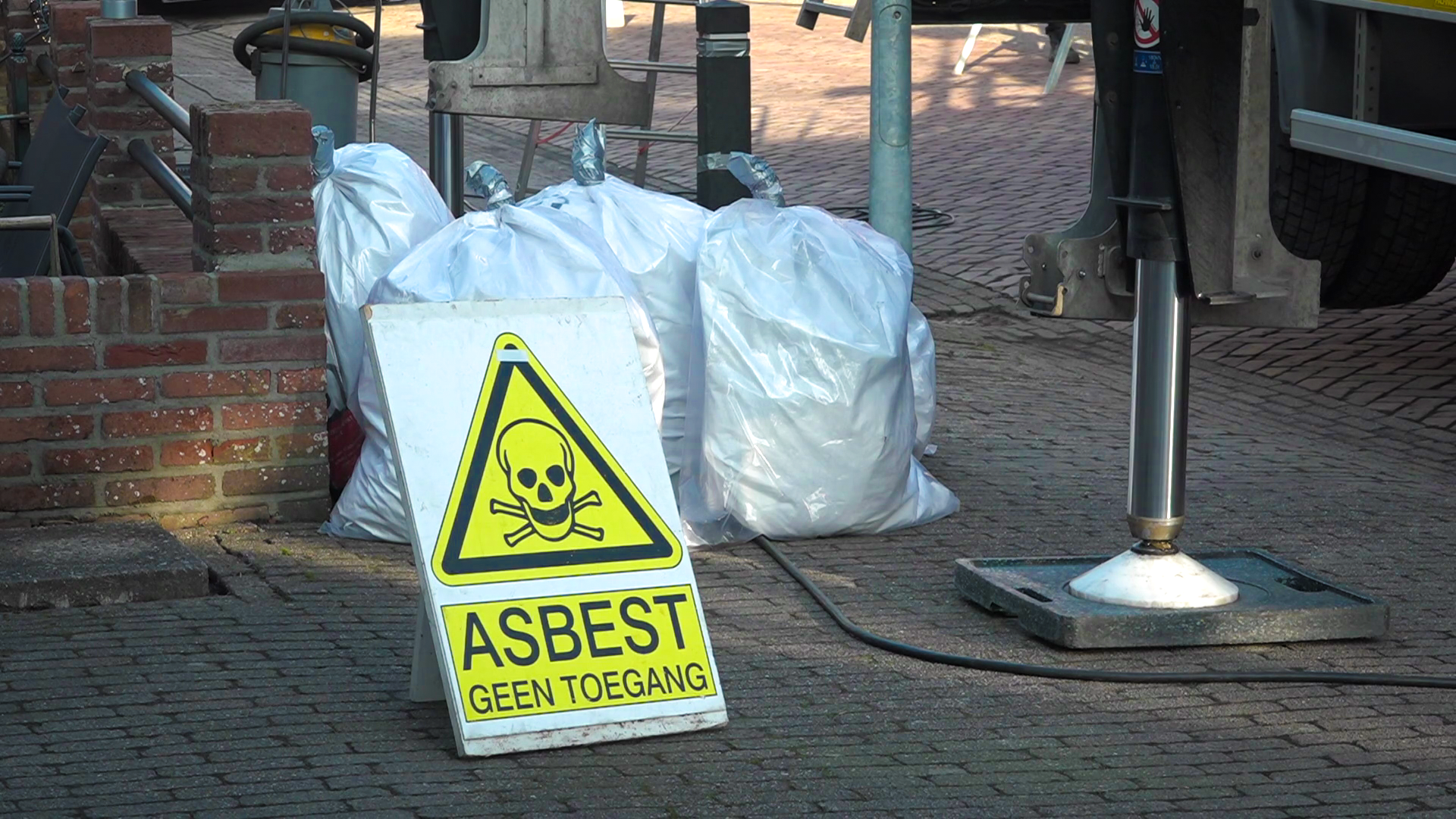 Waarschuwingsbord met "Asbest Geen Toegang" naast witte vuilniszakken op straat.