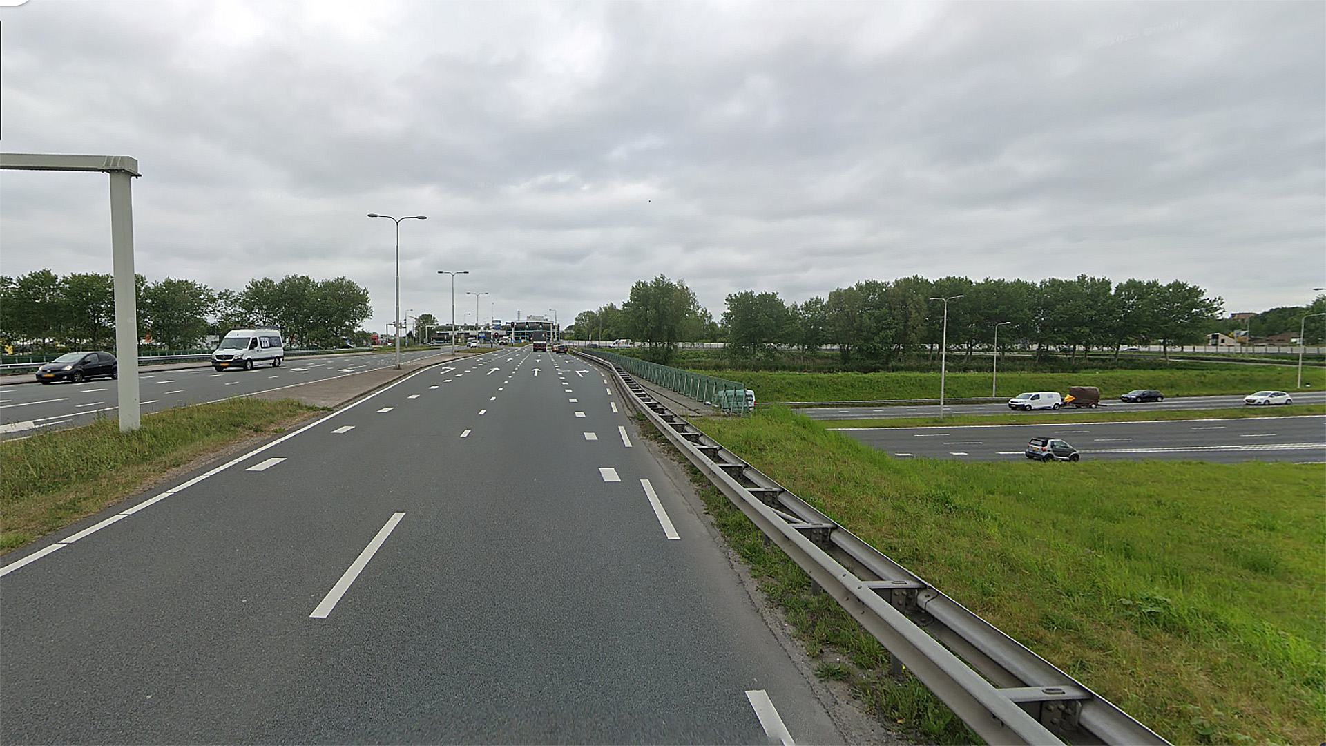 Snelweg met meerdere rijstroken, auto's, en een grasstrook aan de zijkant onder een bewolkte hemel.