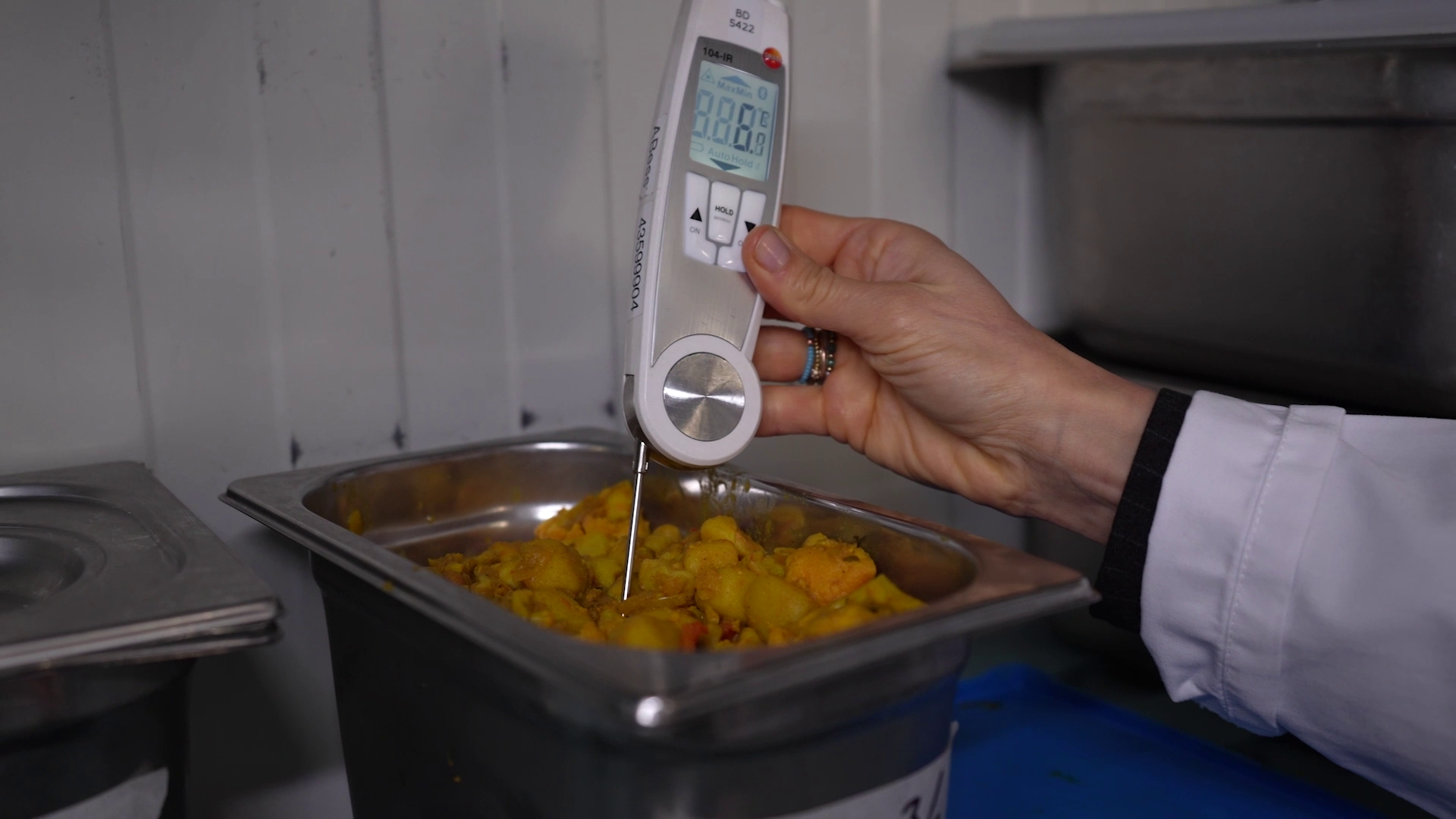 Een persoon meet de temperatuur van gekookt voedsel in een metalen bak met een thermometer.