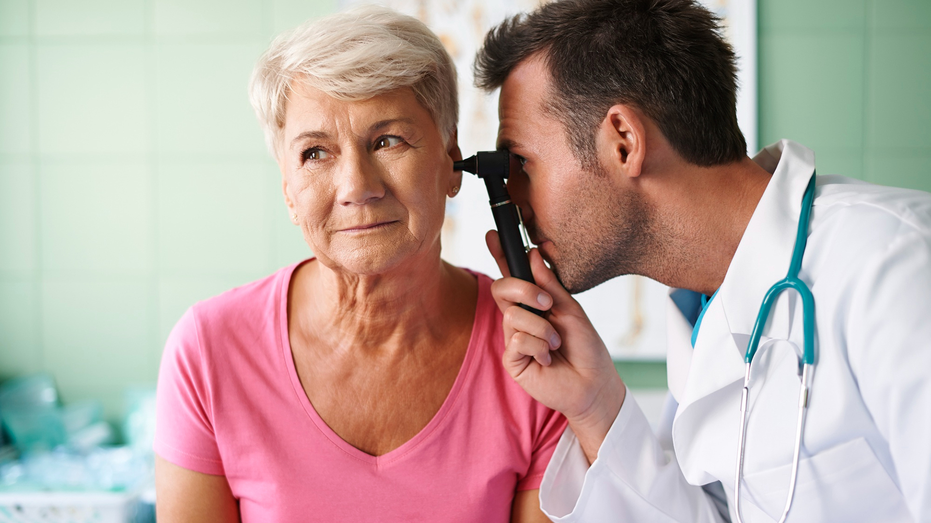 Arts in witte jas onderzoekt het oor van een oudere vrouw met een otoscoop.