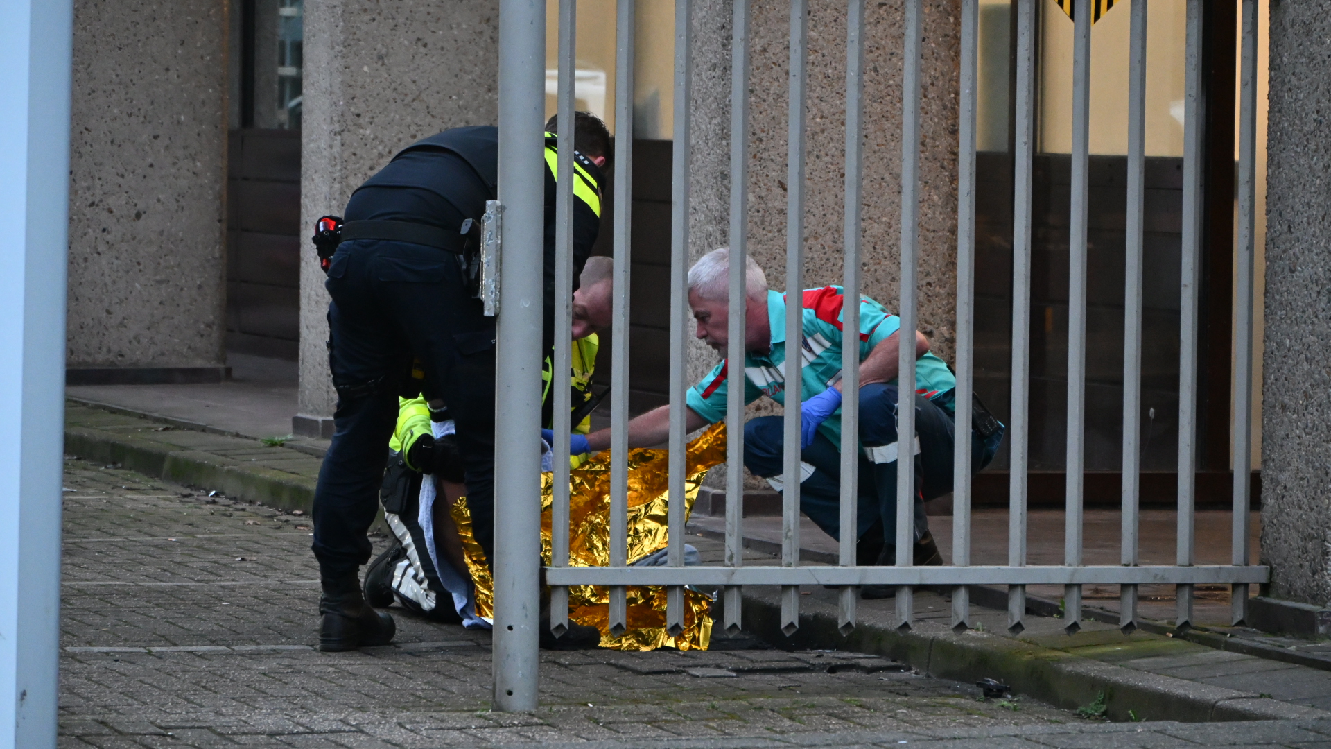 Politieagent en medische hulpverlener zorgen voor een persoon die op de grond ligt, waarbij ze een reddingsdeken gebruiken.