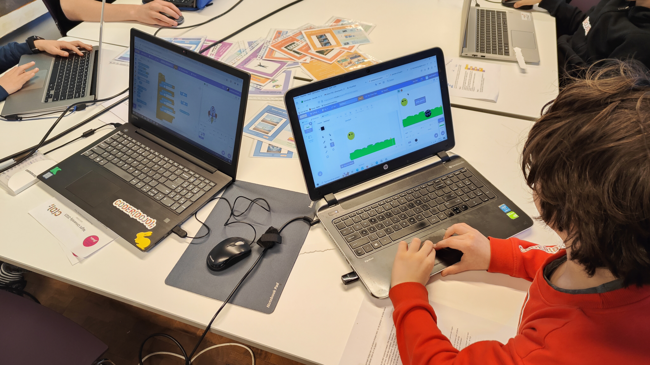 Kinderen werken aan laptops aan een programmeerproject in een klaslokaal.
