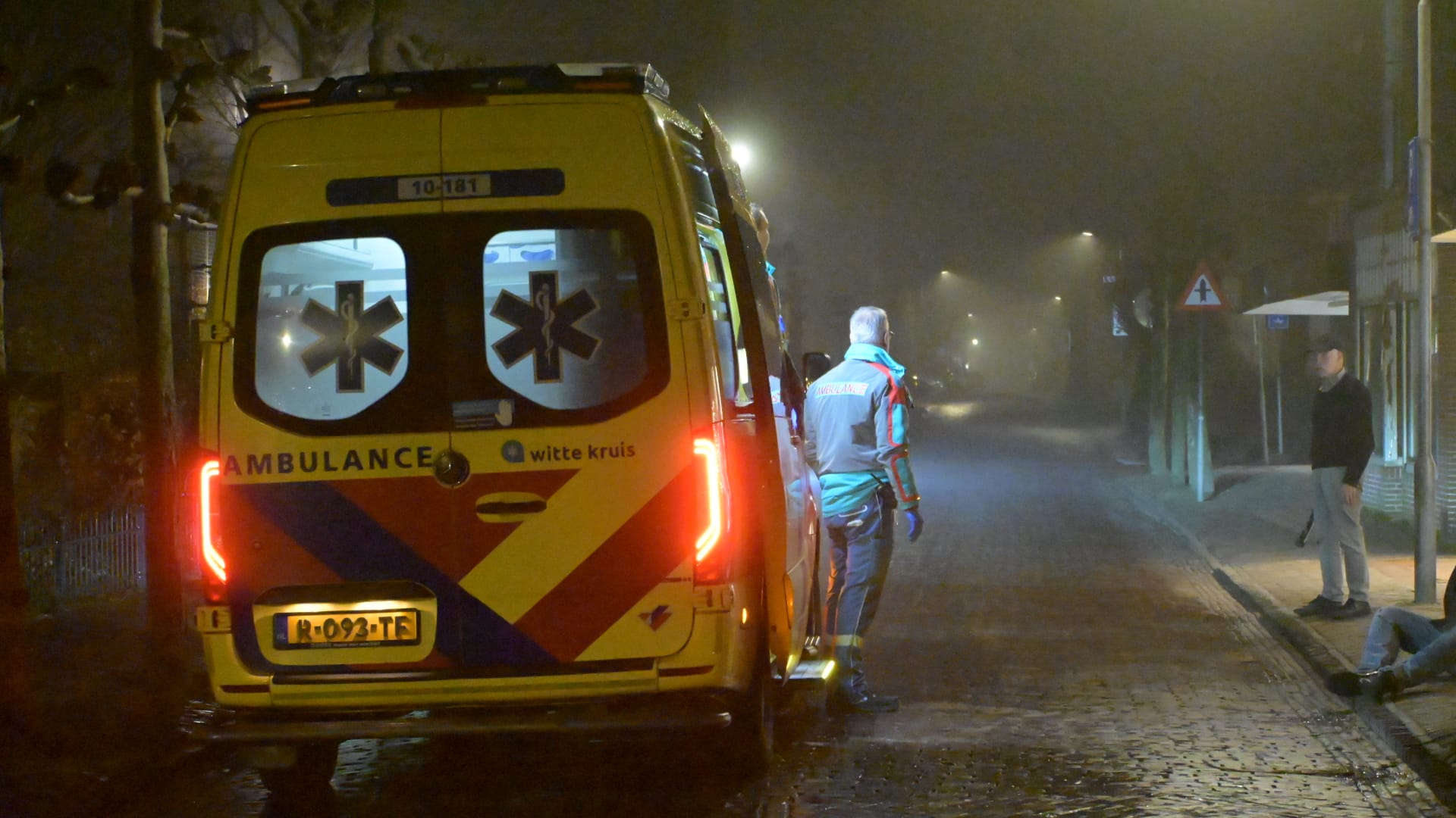 Een ambulance staat geparkeerd op een mistige straat met een paramedicus die naast het voertuig staat.