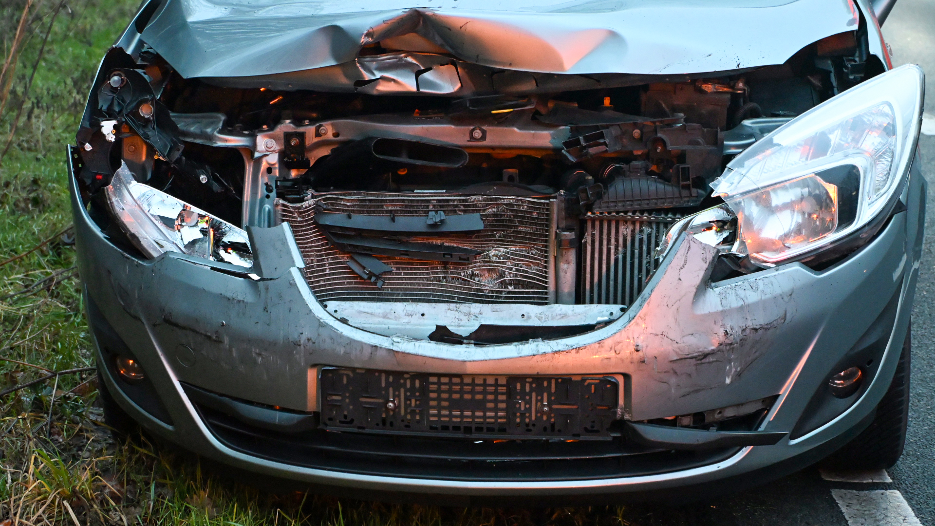 De voorkant van een beschadigde auto met een gedeukt en kapot front en ontbrekende onderdelen.