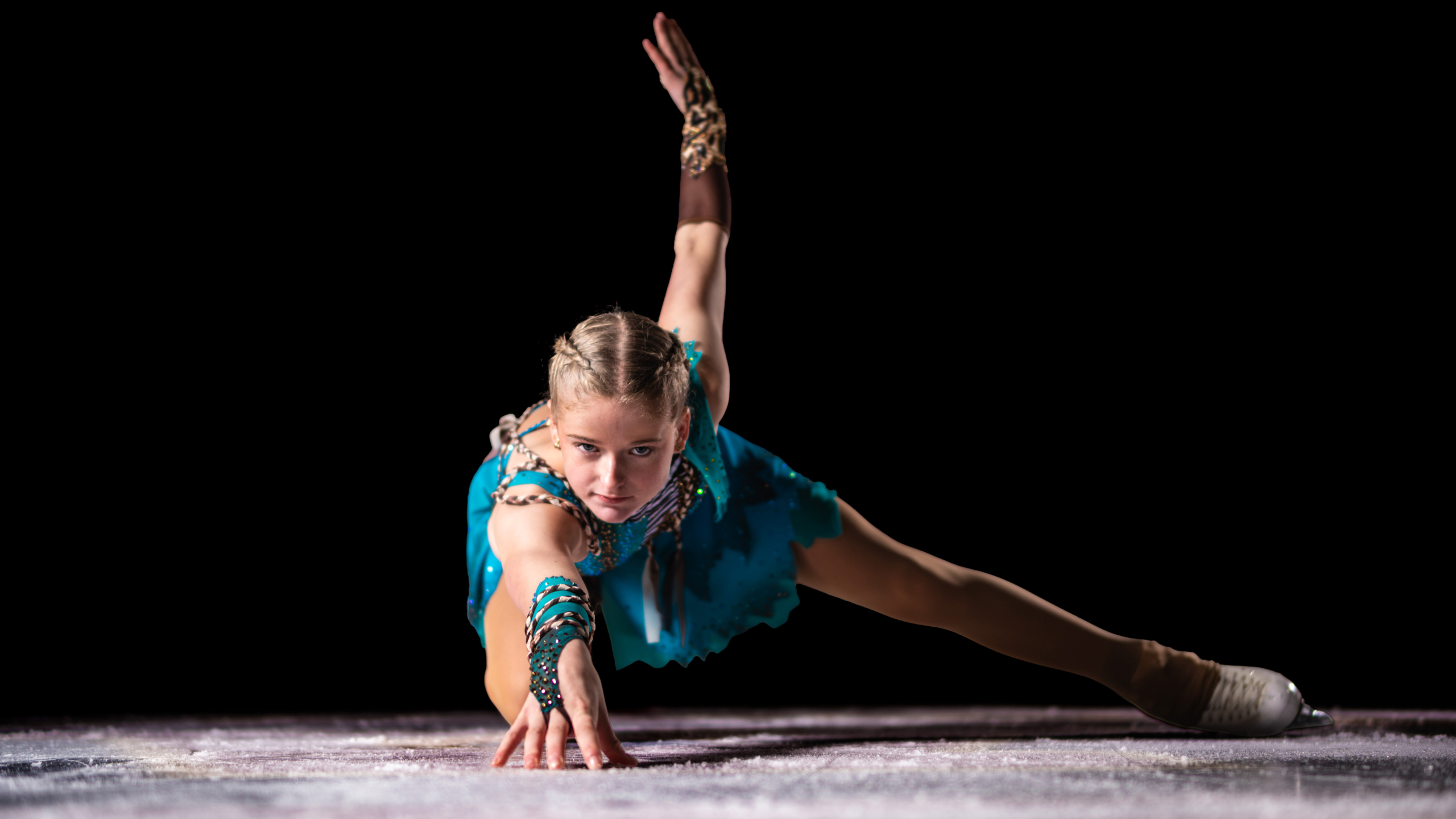 Kunstschaatser in blauwe jurk doet een artistieke pose met een uitgestrekte arm op het ijs.