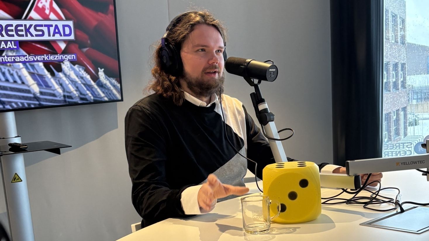 Persoon met een koptelefoon en microfoon in een radiostudio, met een scherm dat "Streekstad Centraal" toont.