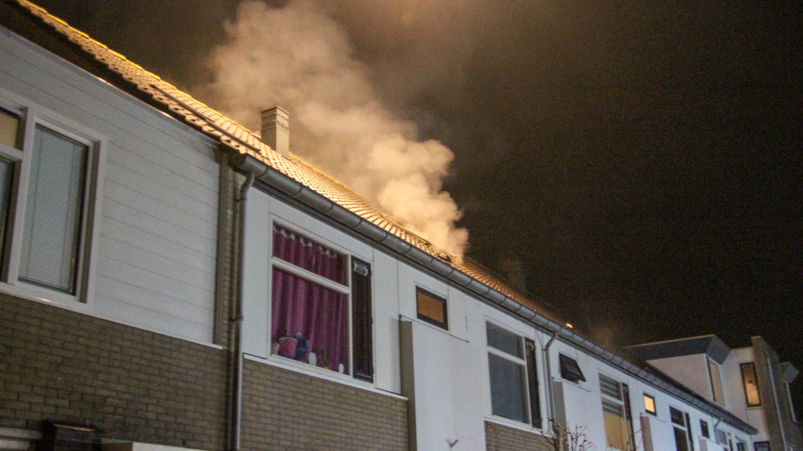 Rook komt uit het dak van een rijtjeshuis onder een donkere hemel.